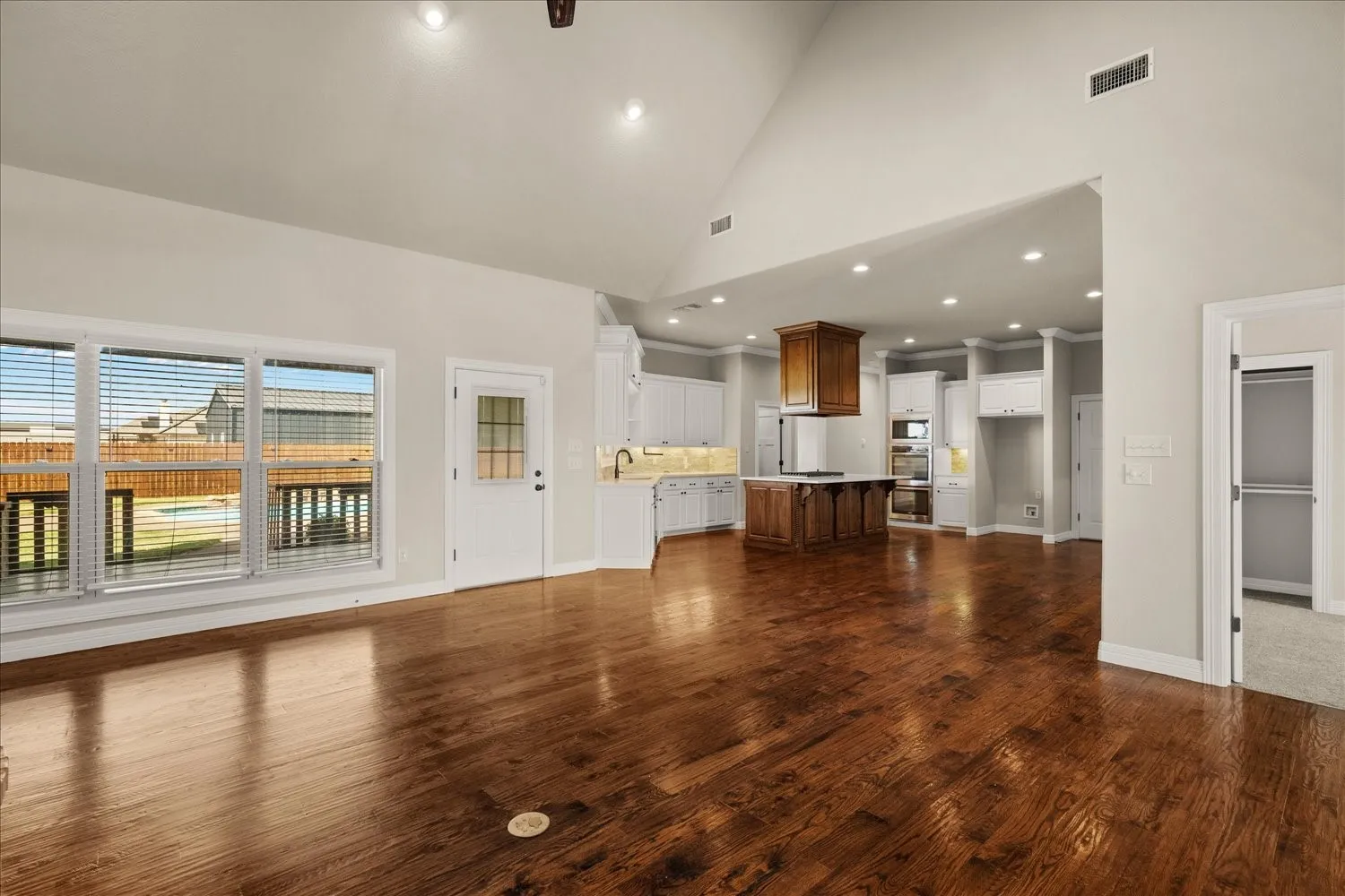 Vaulted ceiling, recessed lighting, wood-finish flooring, white cabinetry, and a kitchen island with a wood base