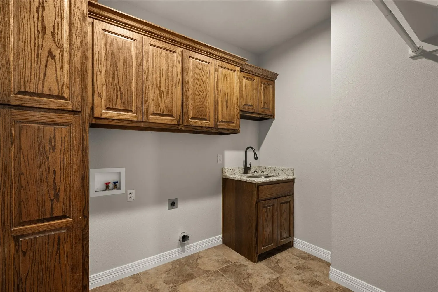 Wood-finish cabinetry, built-in sink with dark-toned faucet, light-toned walls, tiled flooring, and ample storage