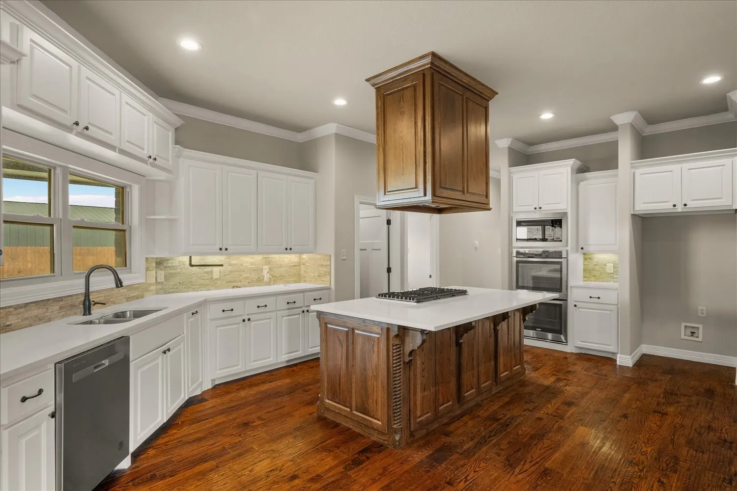 Wood-finish flooring, white cabinetry, a center island with a cooktop, a built-in oven, and a built-in microwave