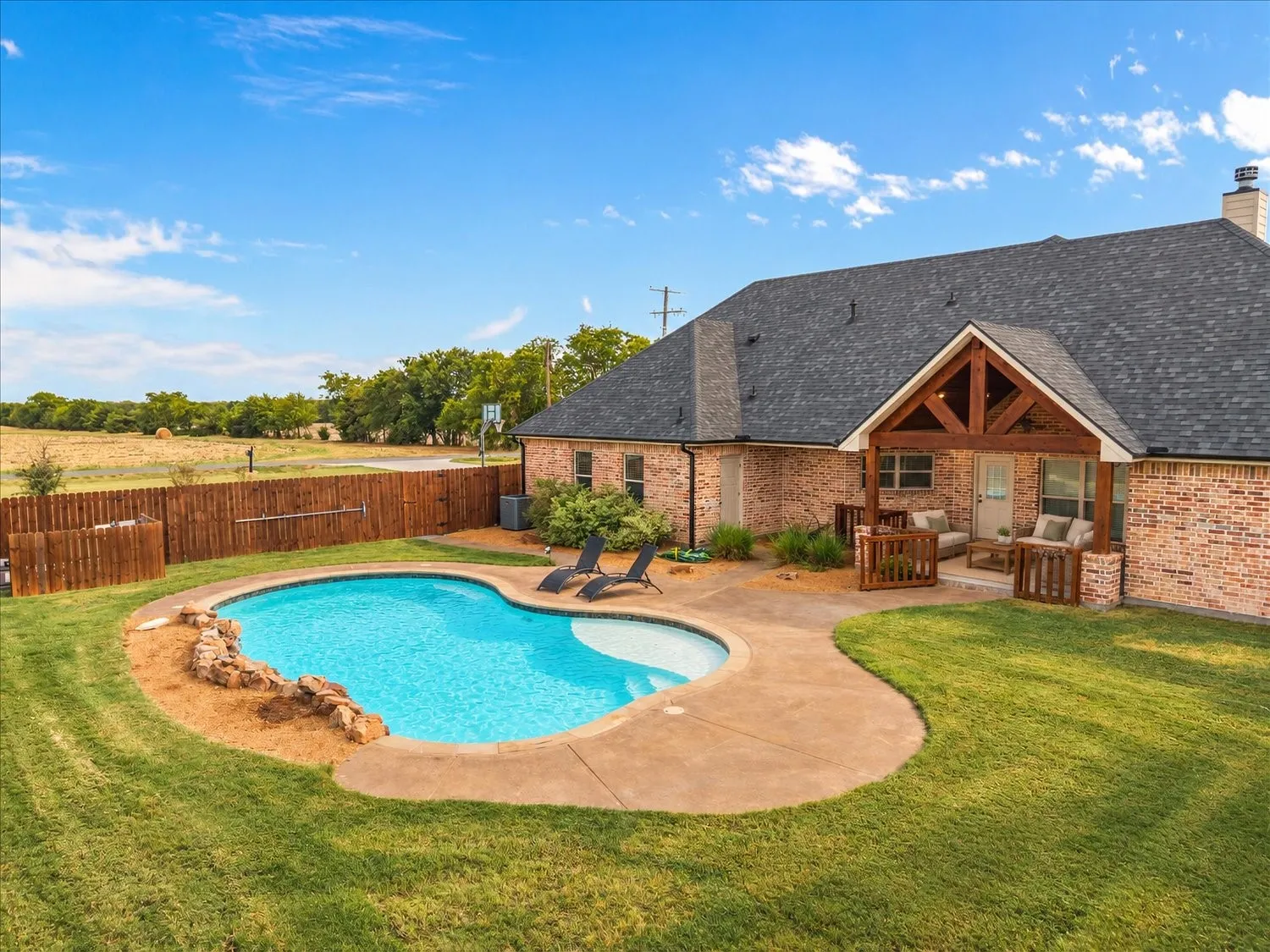 Brick exterior with a gabled roofline, a built-in covered patio, and a fenced backyard featuring a swimming pool with concrete decking