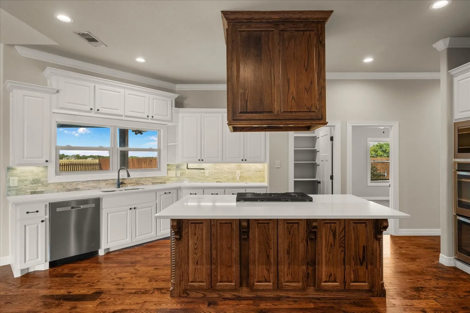 Gourmet kitchen with wood-finish flooring, white cabinetry, a large center island with a cooktop, and stainless steel appliances including a built-in oven and dishwasher