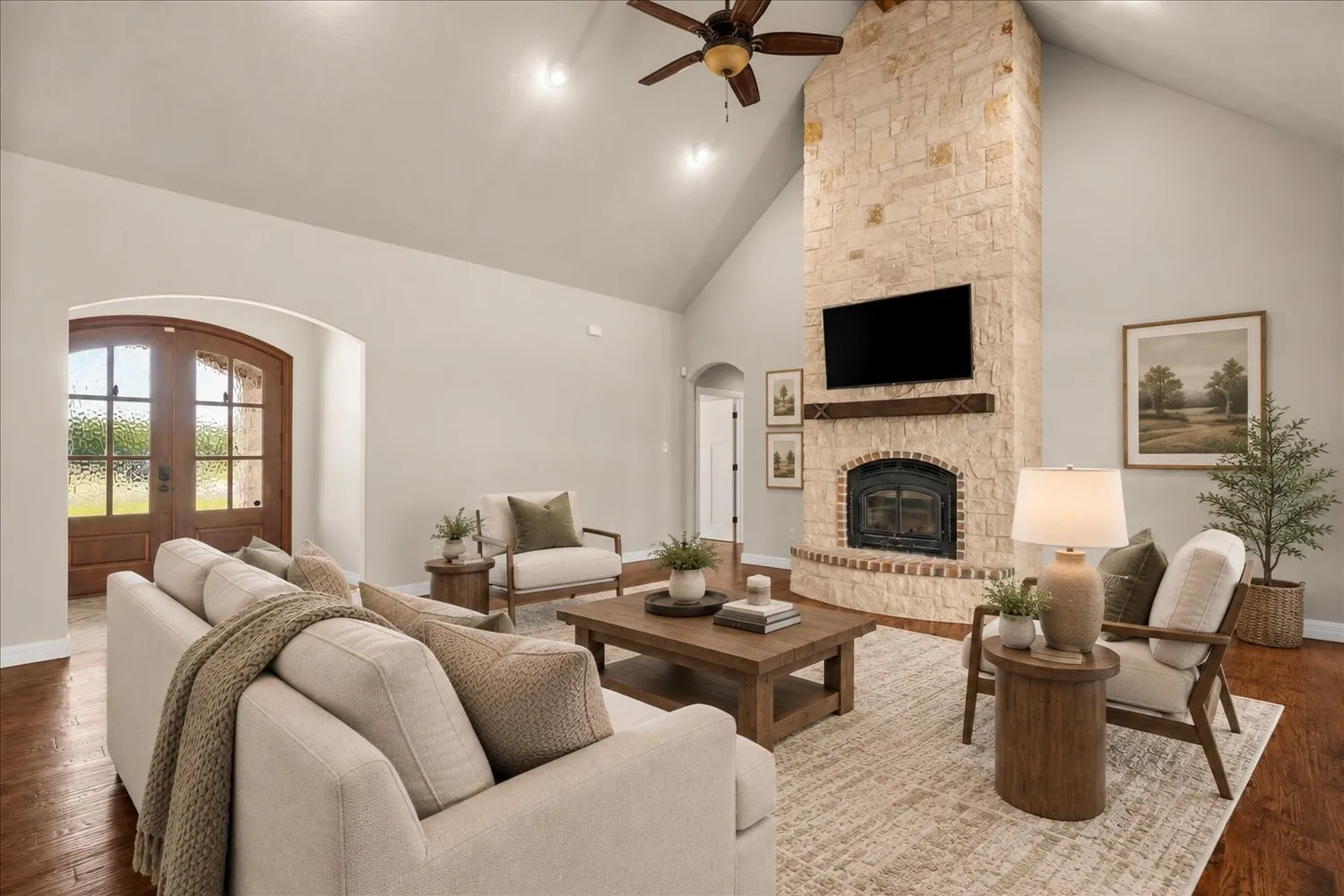 Vaulted ceilings, a stone fireplace with a wood-finish mantel, and wood-finish flooring