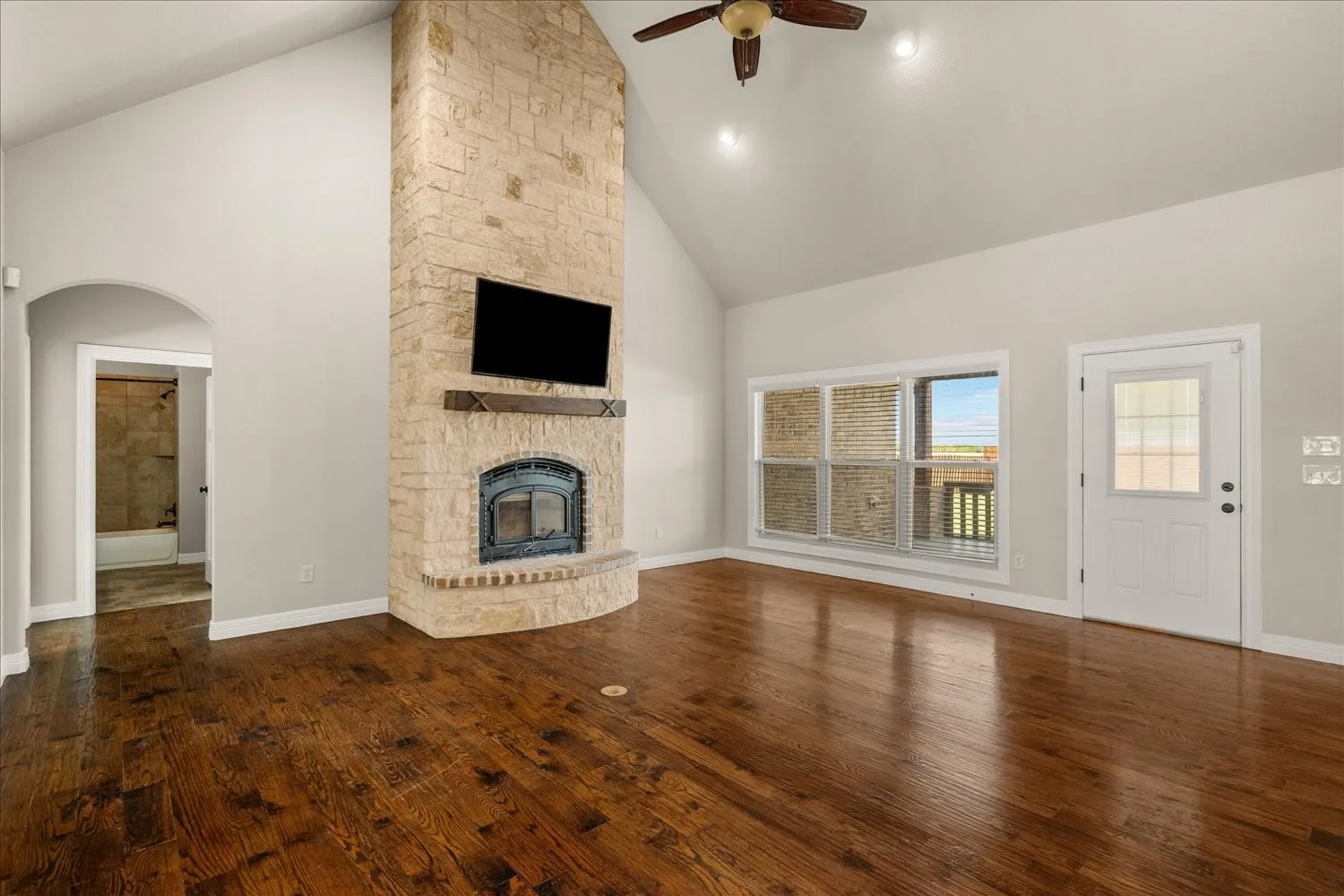 Vaulted ceiling, stone-clad fireplace with hearth, wood-finish flooring, ceiling fan, and exterior access