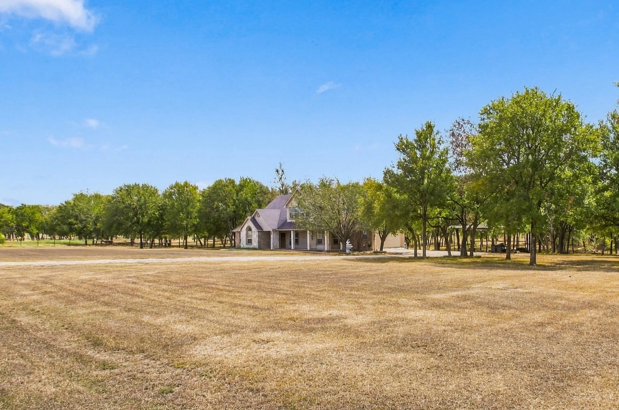 Expansive field with a distant home featuring a gabled roofline and a columned porch