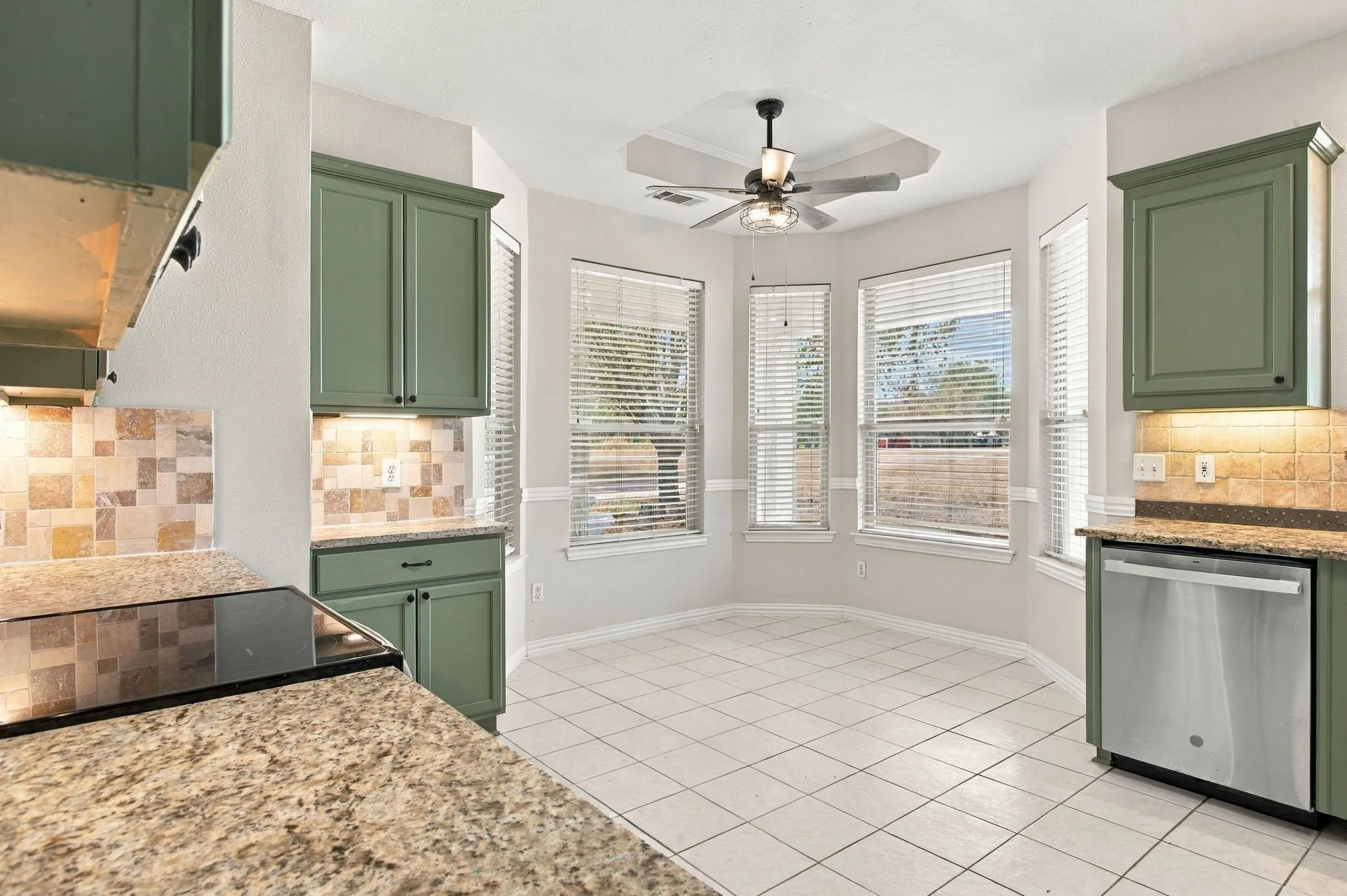 Kitchen featuring granite-look countertops, subway tile backsplash, green cabinetry, and stainless steel dishwasher