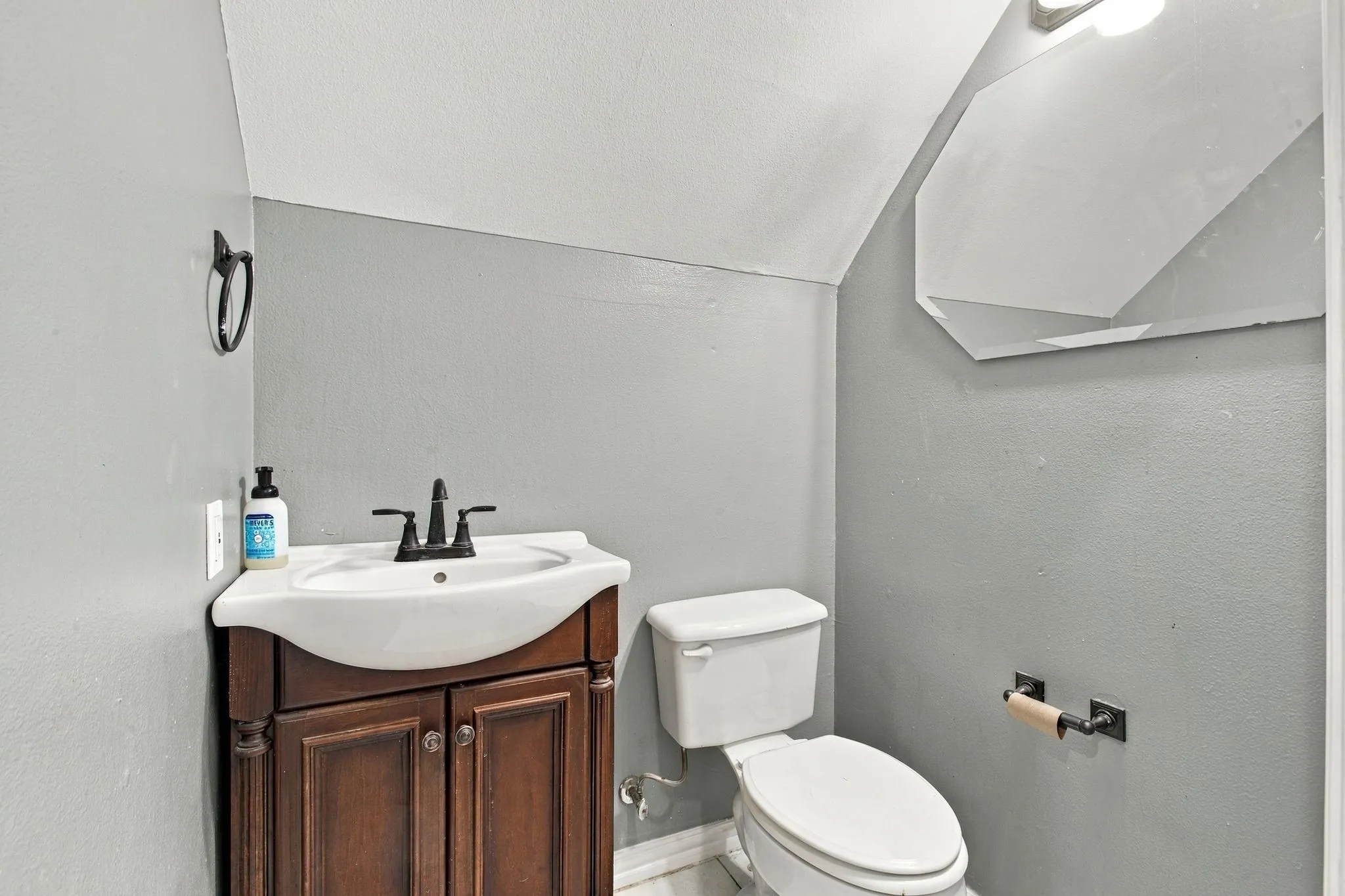 Compact bathroom featuring a wood-finish vanity with a white basin and matte black faucet, a white toilet, and a geometric wall mirror