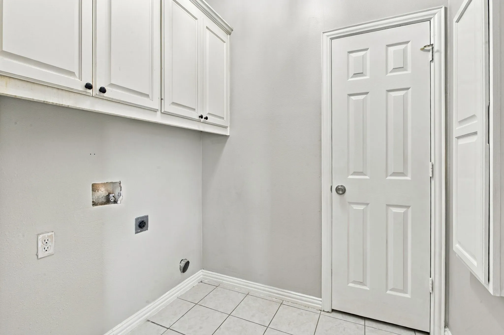 White shaker-style cabinetry with black hardware, ceramic tile flooring, and a paneled door