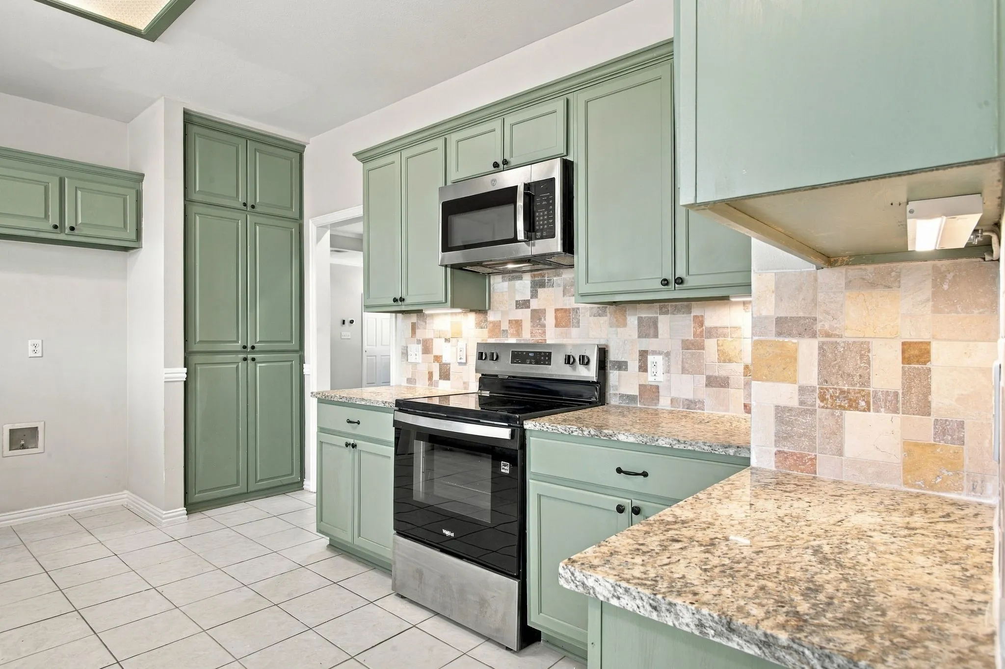 Kitchen featuring light green cabinetry, stainless steel oven with an electric cooktop, stainless steel microwave, stone backsplash, and granite-style countertops
