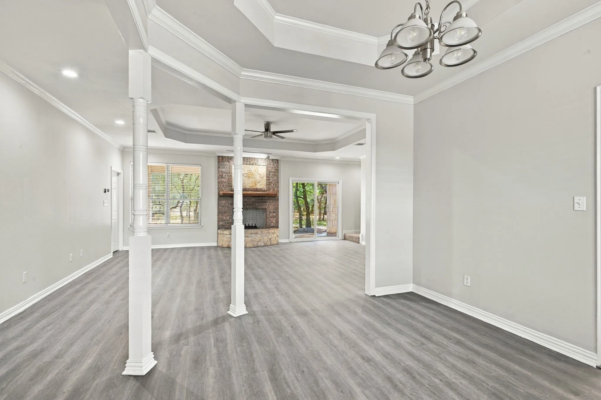 Expansive living area with wood-finish flooring, tray ceilings, recessed lighting, and a brick fireplace