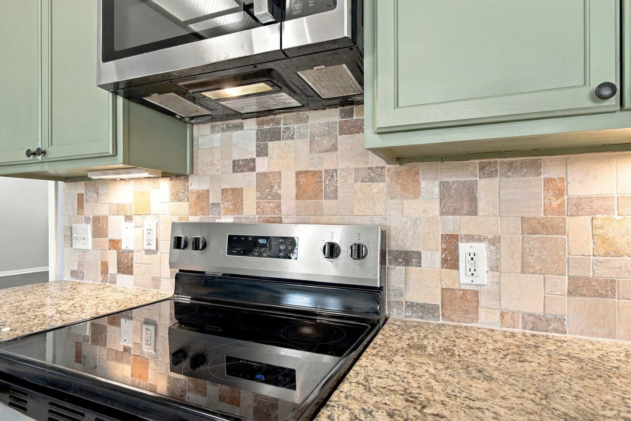 Stainless steel microwave and range, tile backsplash, laminate countertops, and painted cabinetry