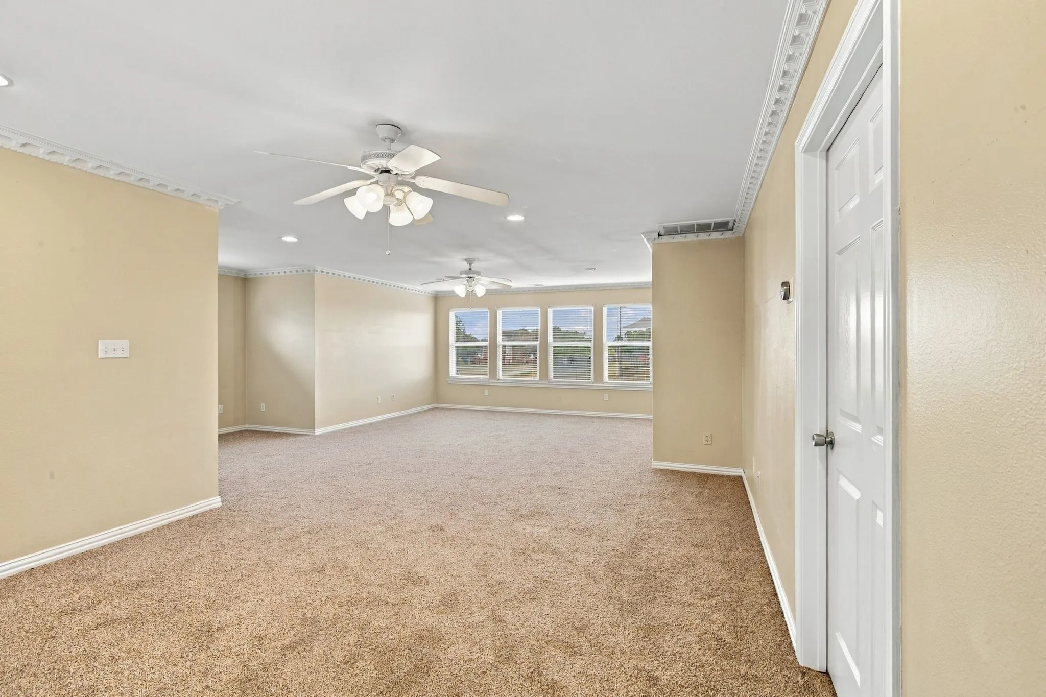 Spacious room featuring multiple windows, recessed lighting, crown molding, and two ceiling fans