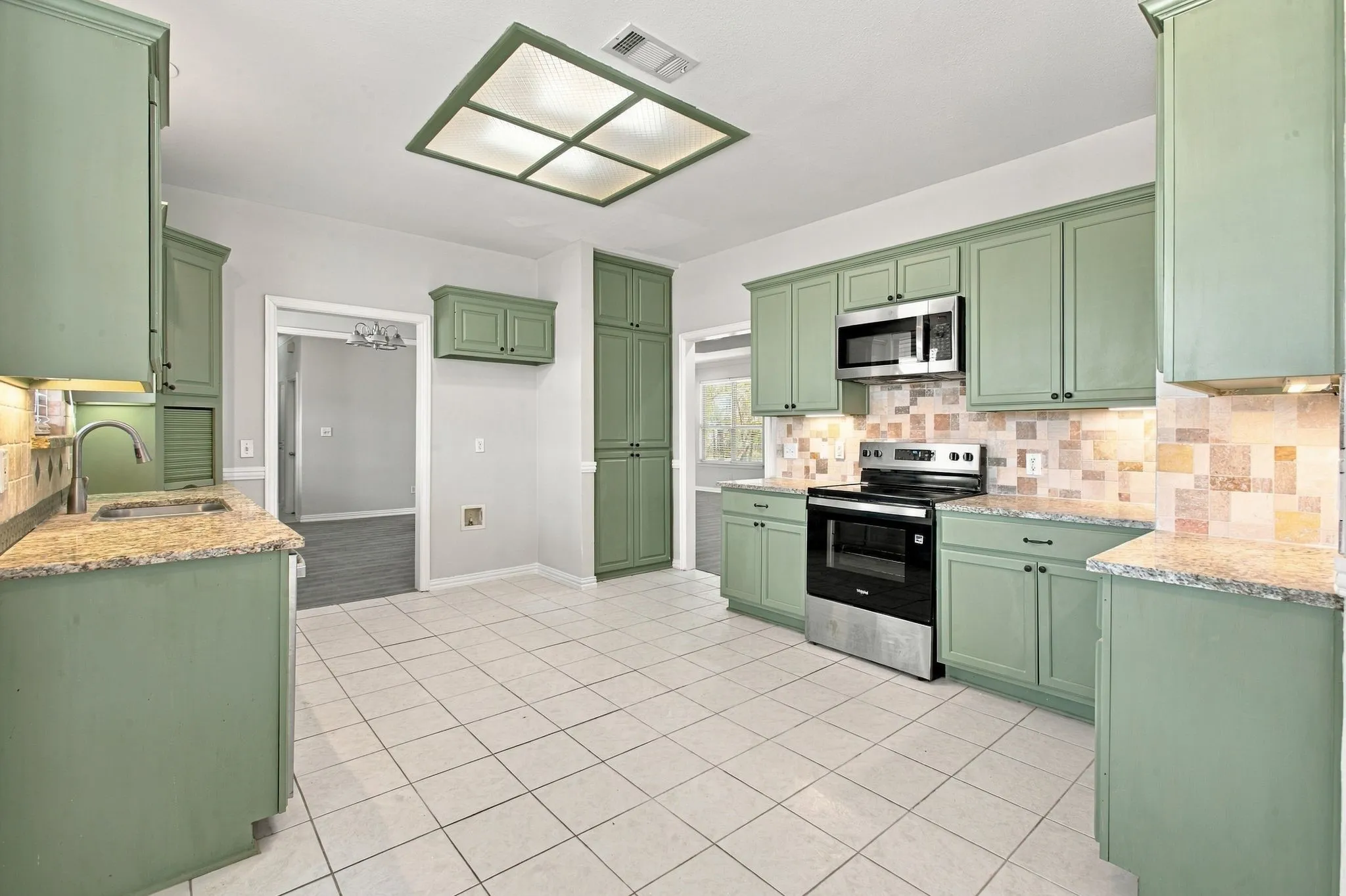 Kitchen featuring light green cabinetry, stainless steel appliances, patterned backsplash, light-toned countertops, and square tile flooring