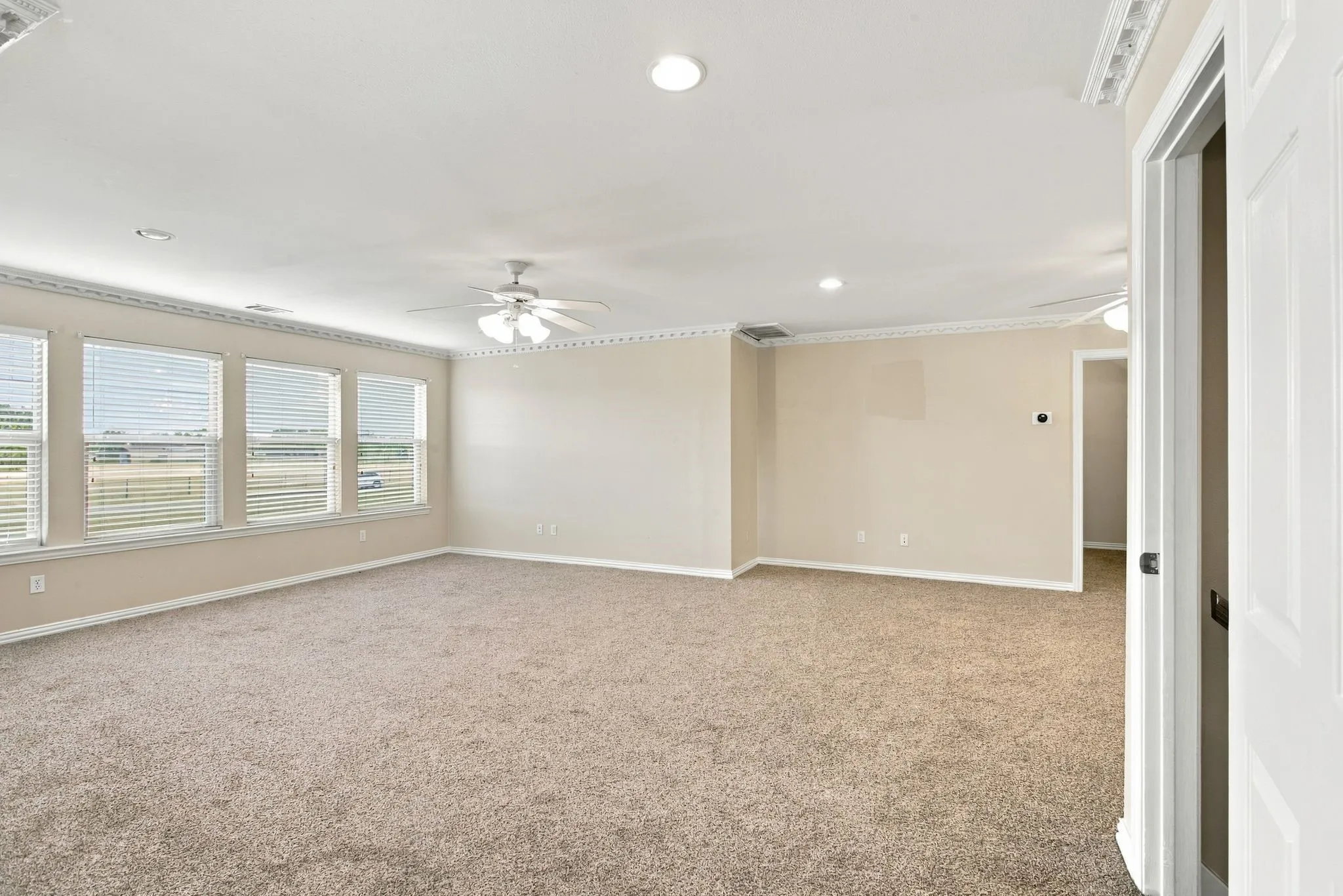 Spacious room with carpeted flooring, multiple windows featuring blinds, recessed lighting, crown molding, and ceiling fans