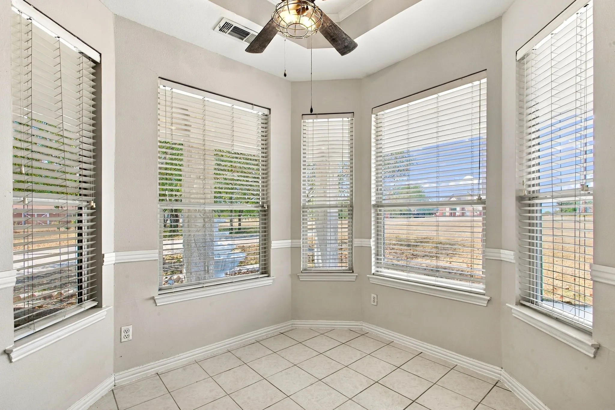 Recessed ceiling with an overhead fan, tiled flooring, multiple windows with blinds, and white wall trim