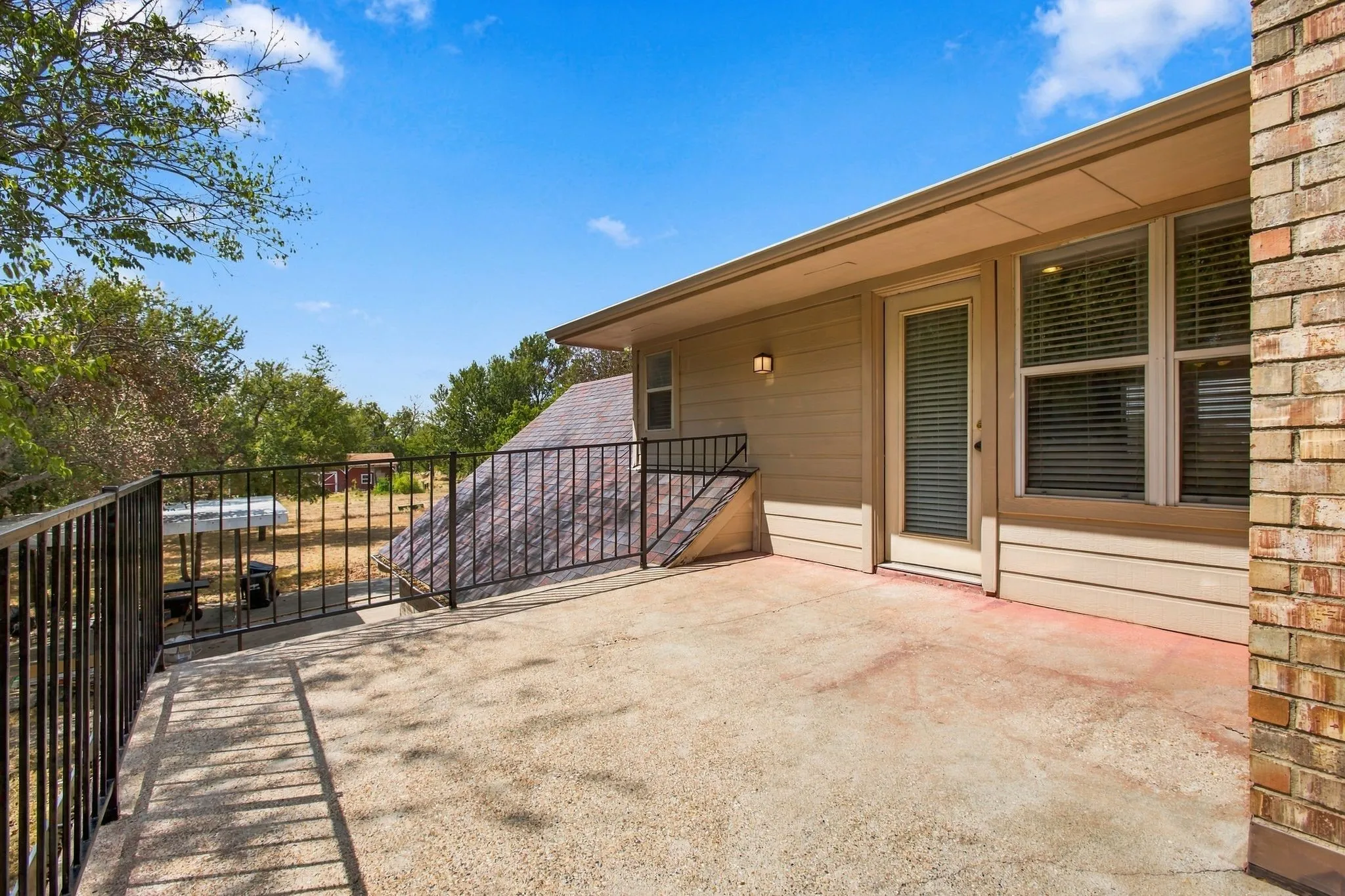Concrete patio with black metal railings, vinyl siding, and brick accents