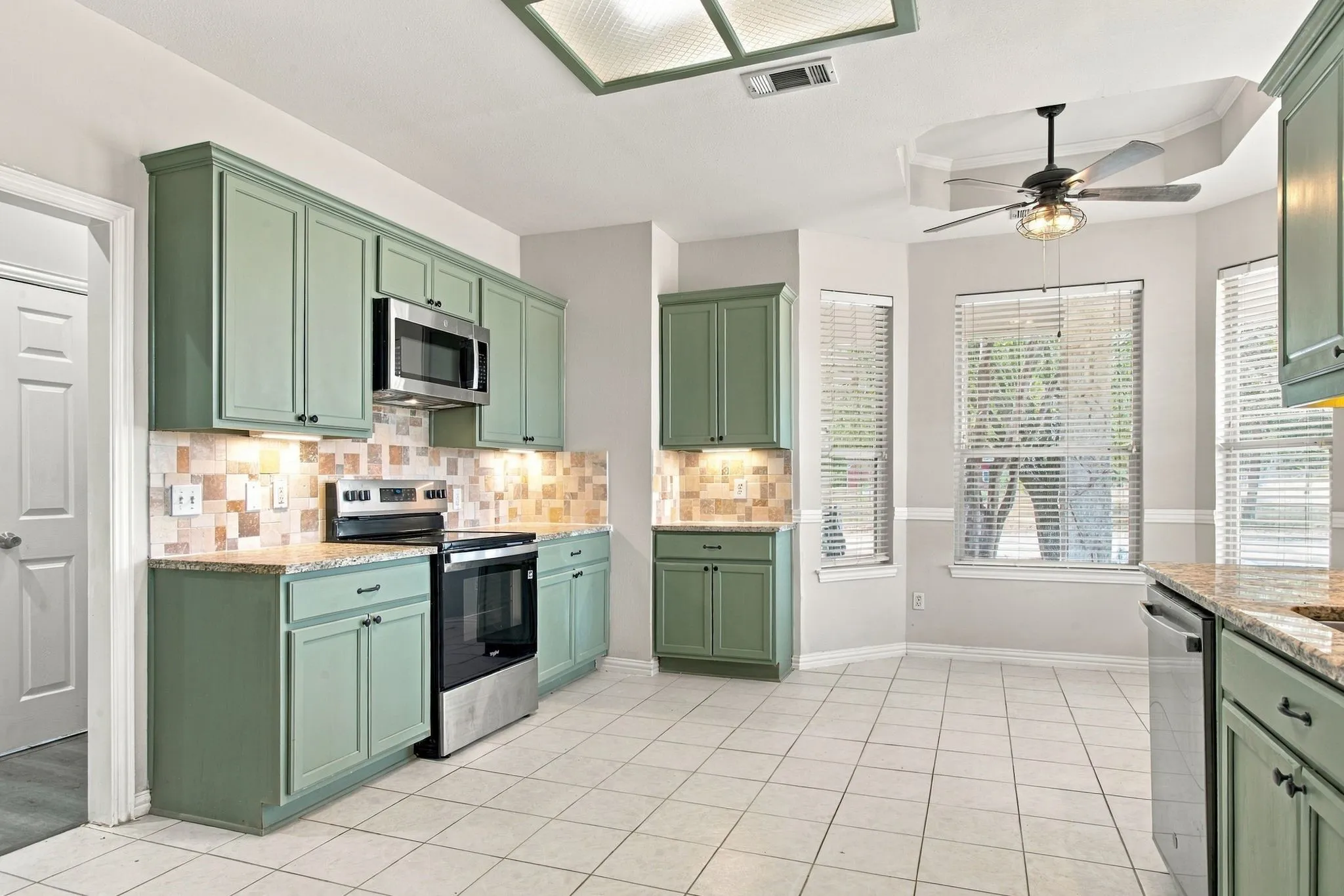 Kitchen featuring green cabinetry, stainless steel appliances, tiled backsplash, and granite countertops