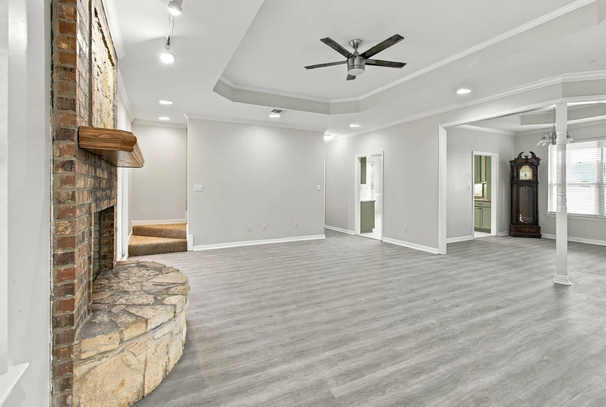 Spacious interior with wood-finish flooring, a brick fireplace with stone hearth, and a tray ceiling with a ceiling fan