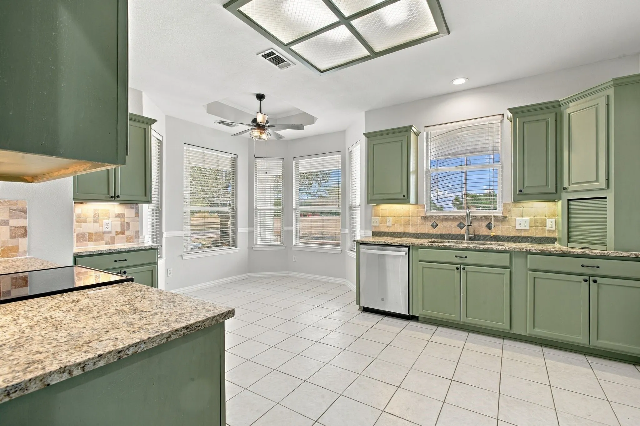 Kitchen featuring green cabinetry, light-toned countertops, a mosaic tile backsplash, and a stainless steel dishwasher