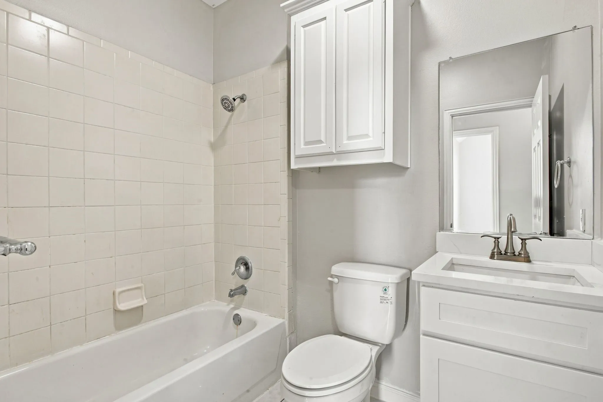 White subway tile tub surround, white vanity with integrated sink, wall-mounted mirror, and white upper cabinetry