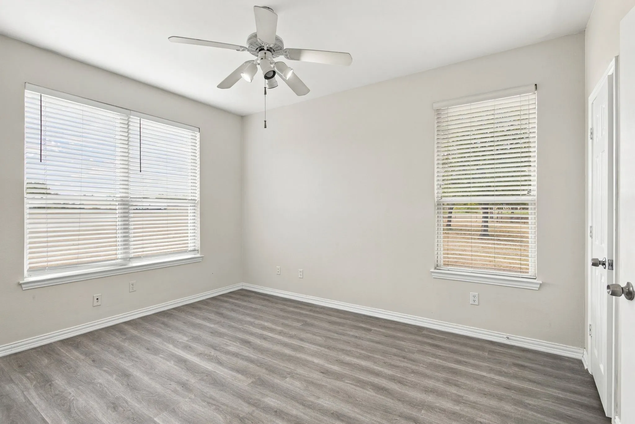 Spacious room featuring wood-finish flooring, light neutral wall paint, and multiple windows with blinds