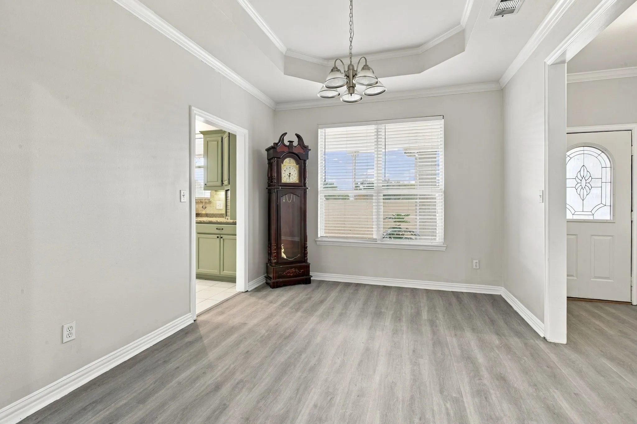 Tray ceiling with crown molding, wood-finish flooring, and a decorative front door with an arched window
