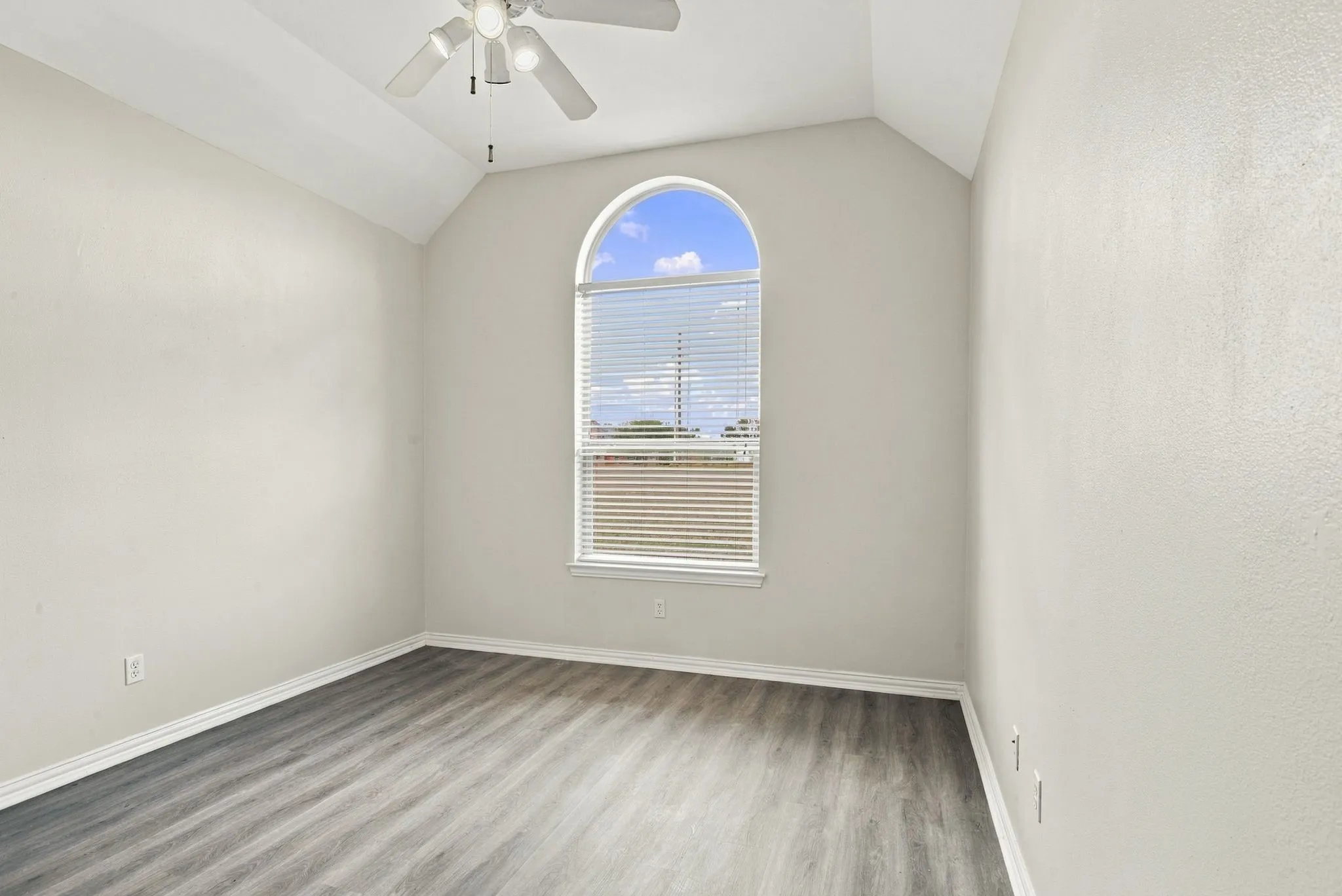 Vaulted ceiling with an attached ceiling fan, arched window with horizontal blinds, wood-finish flooring, and light-colored walls