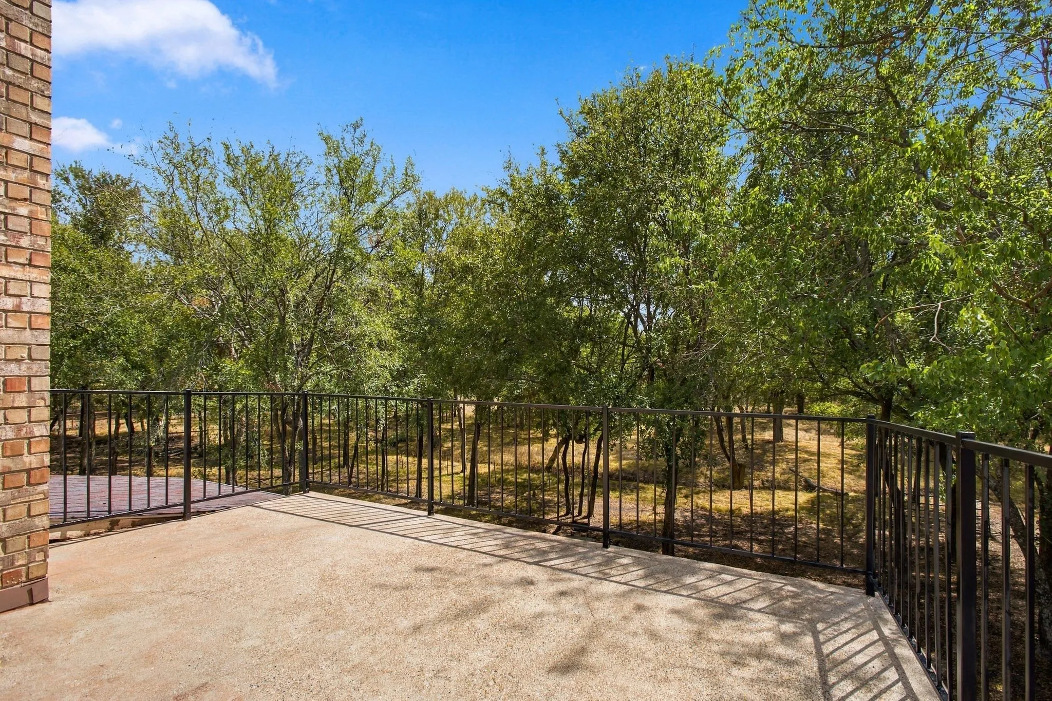 Outdoor patio with concrete flooring, black metal railings, and a brick exterior wall
