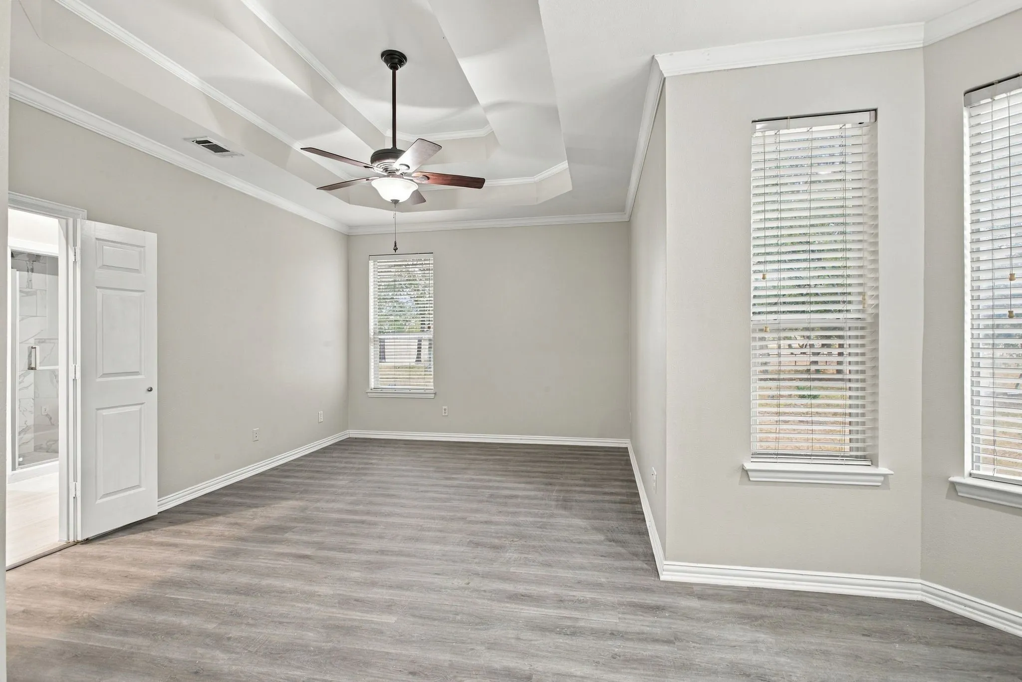 Tray ceiling with a ceiling fan, wood-finish flooring, multiple windows with blinds, and white trim throughout