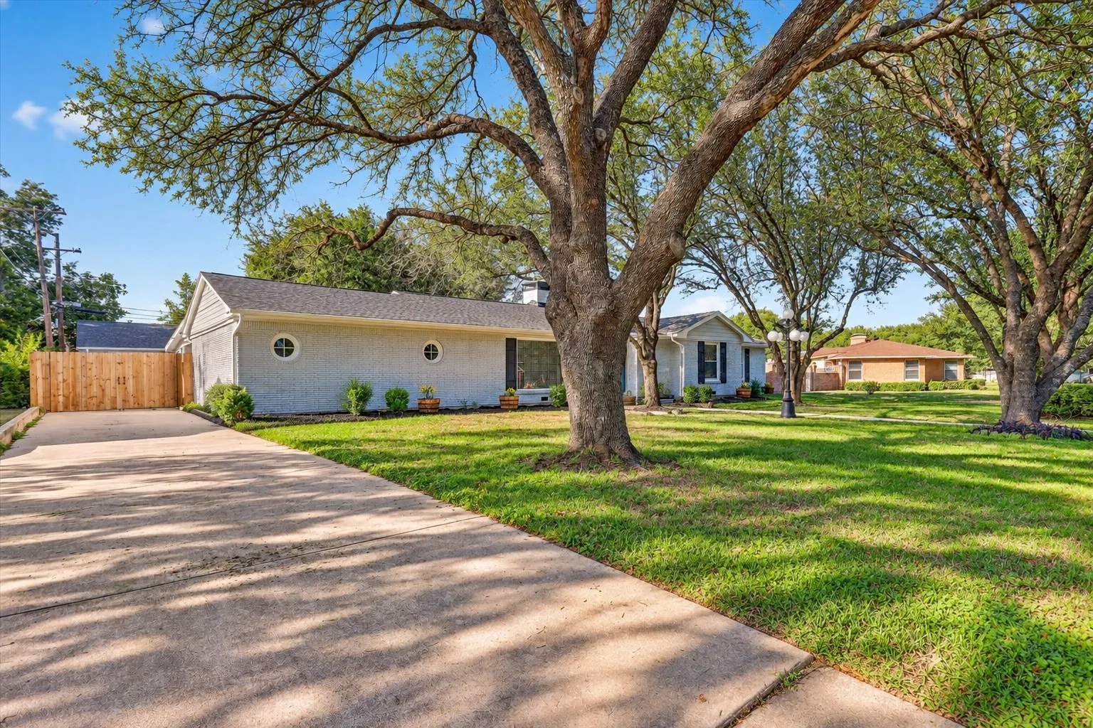 Expansive front yard with mature trees, a concrete driveway, and a wood privacy fence