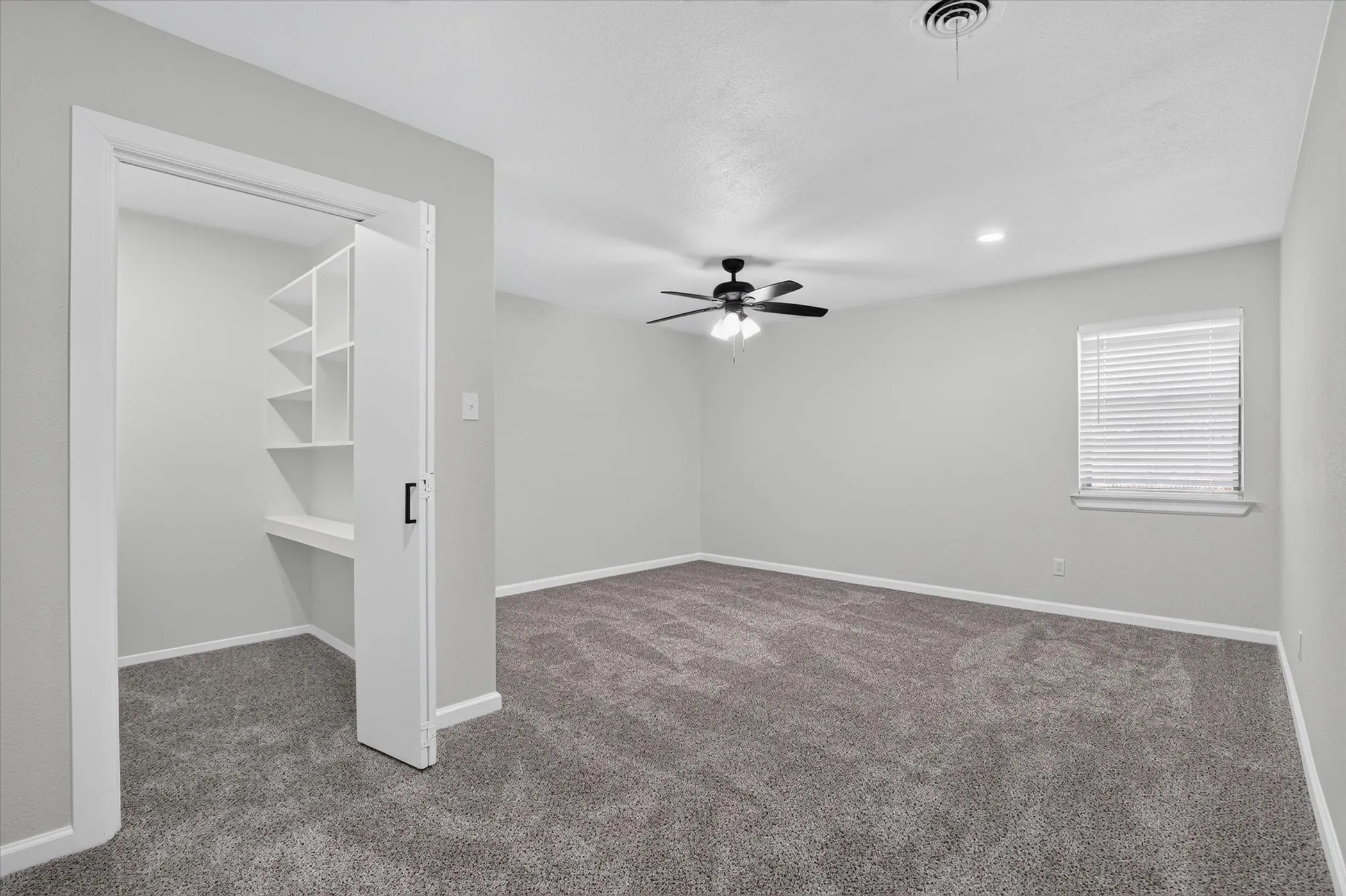 Neutral gray walls, plush gray carpet, ceiling fan, recessed lighting, and built-in shelving
