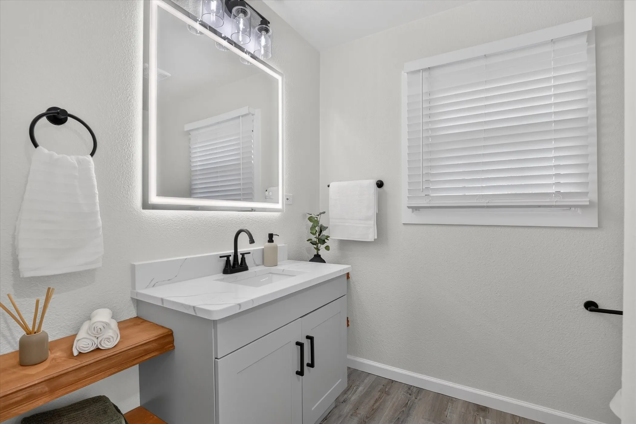 Modern bathroom featuring a floating vanity with wood-finish shelving, white quartz countertop, and matte black hardware