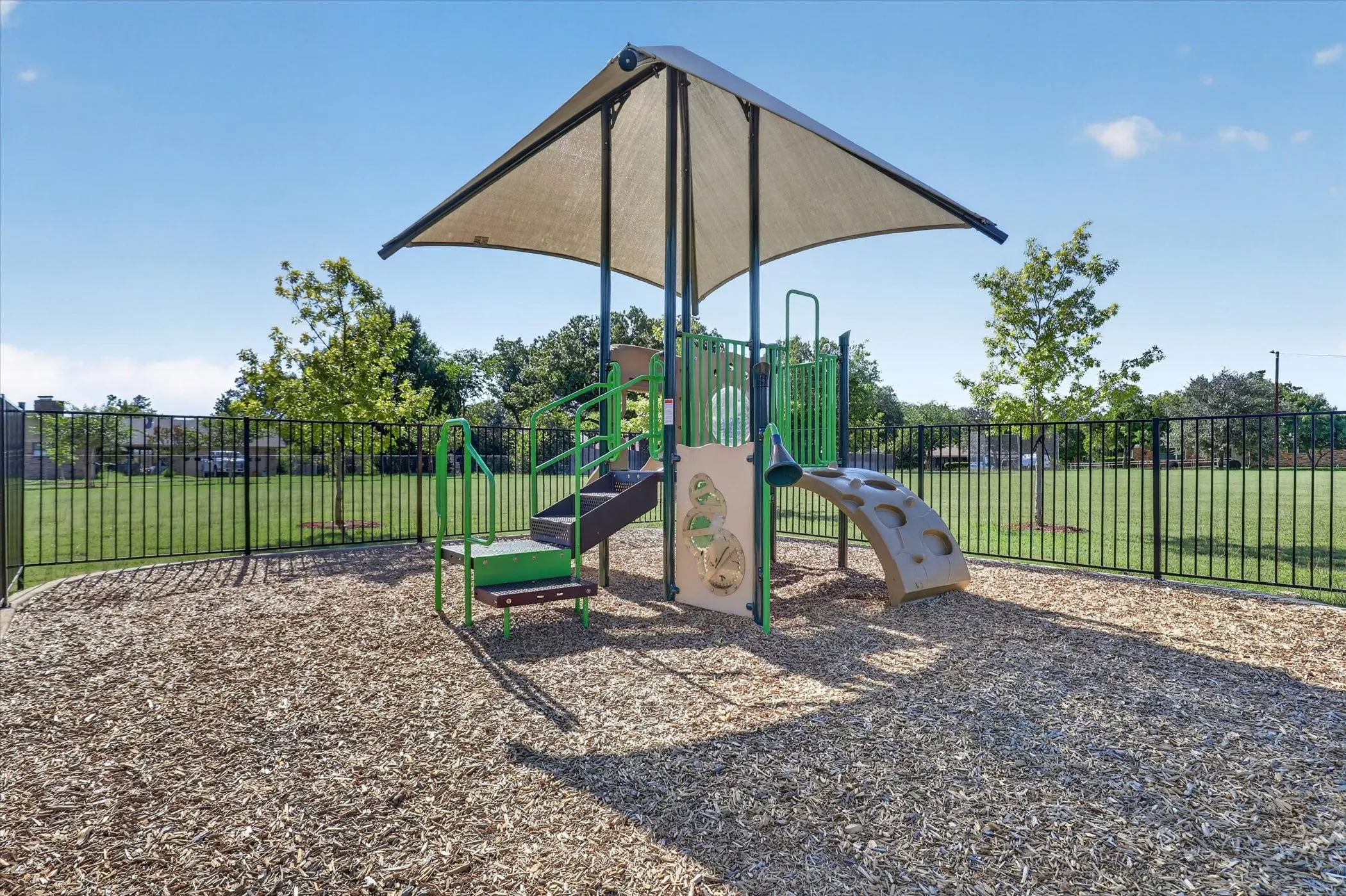 Recreational playground structure featuring a shade canopy, steps, climbing elements, and wood chip surfacing