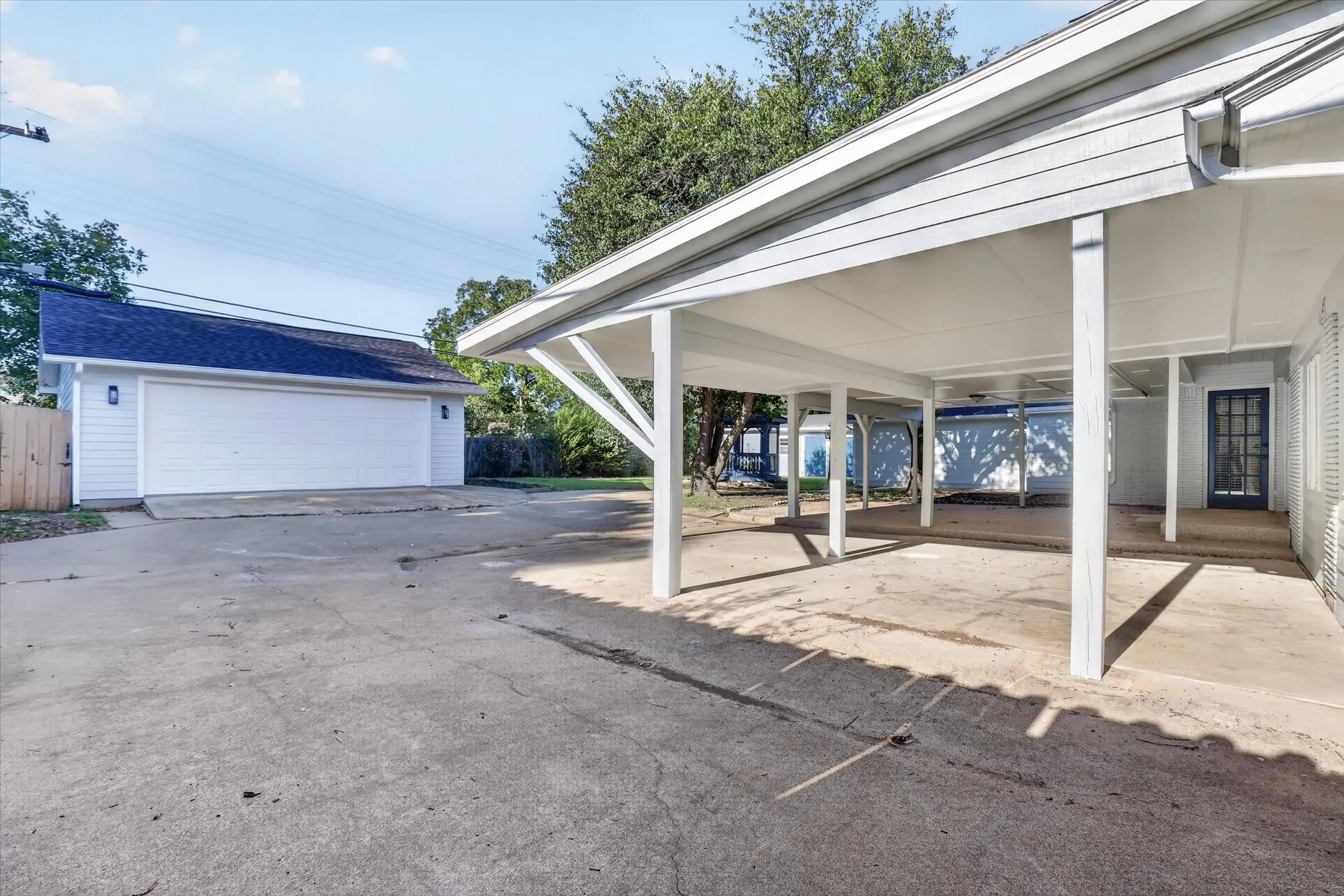 Detached garage with white siding and a dark roof, featuring a double garage door and exterior sconces