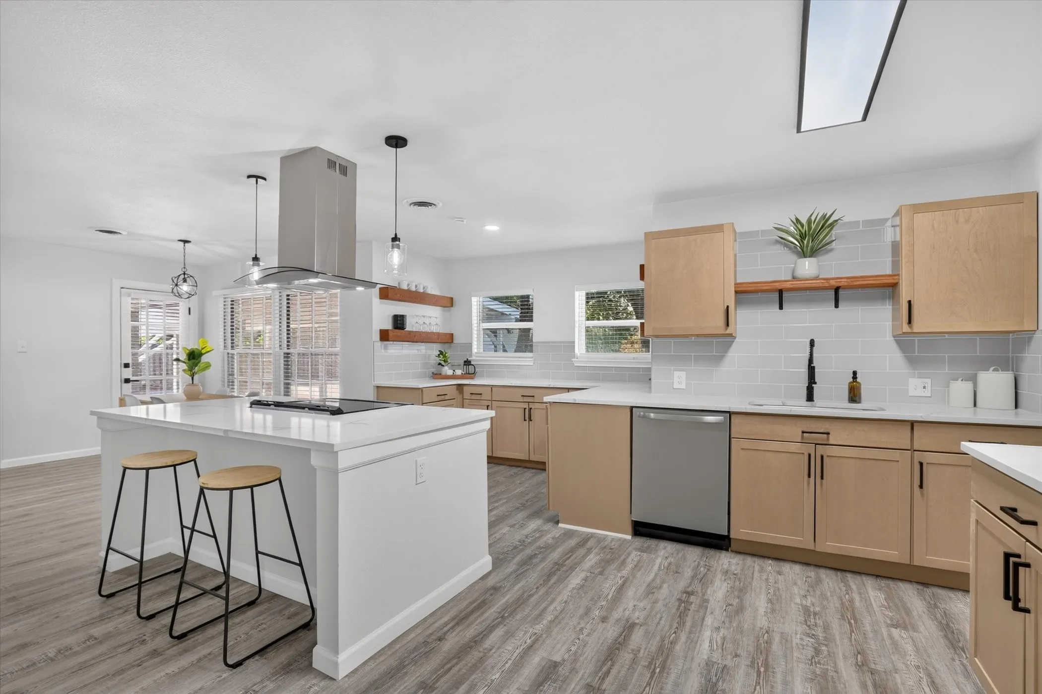 Kitchen featuring wood-finish cabinetry, light-toned countertops, a stainless steel range hood, light gray subway tile backsplash, and wood-finish flooring