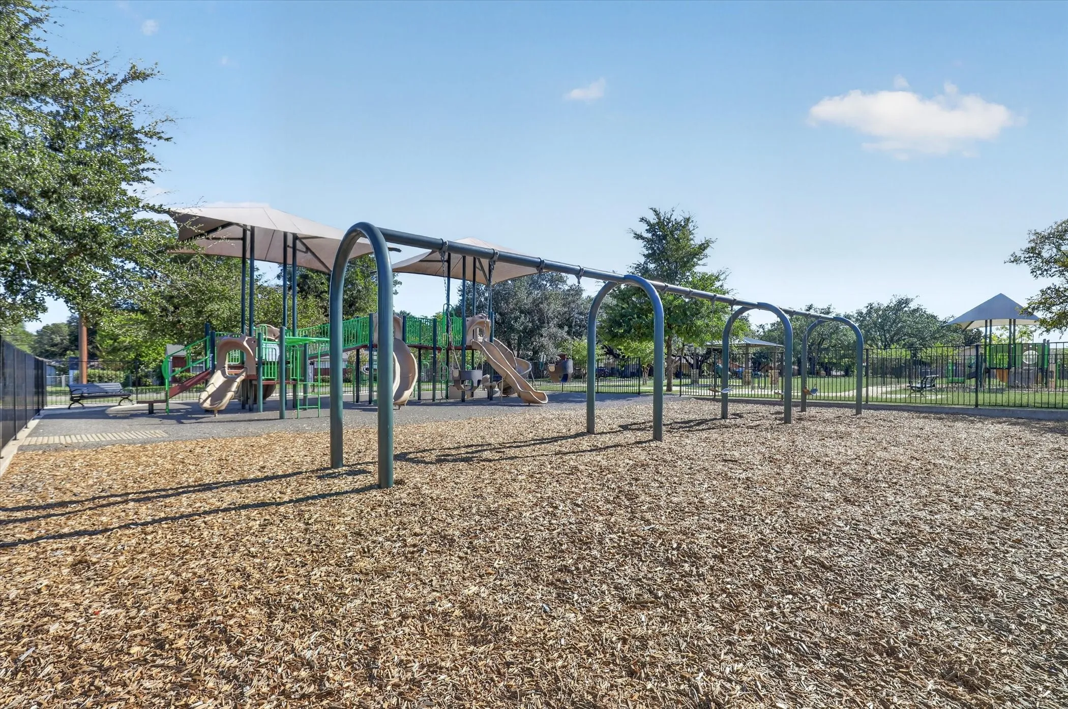 Playground featuring multiple slides, climbing structures, and protective overhead canopies, set on a wood chip surface