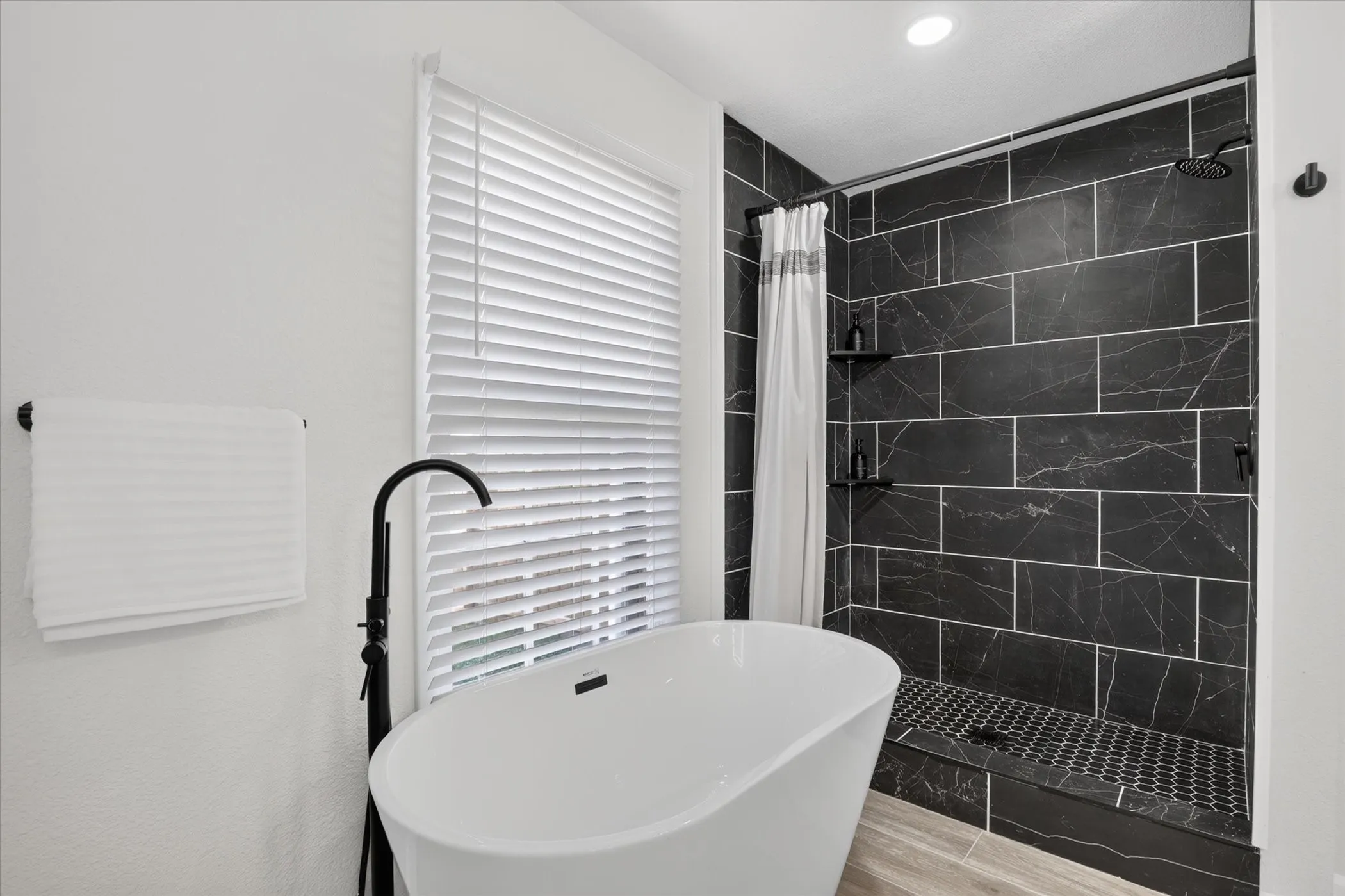 Freestanding soaking tub with a floor-mounted faucet, complemented by a walk-in shower featuring dark subway tile and a dark hexagon tile shower pan