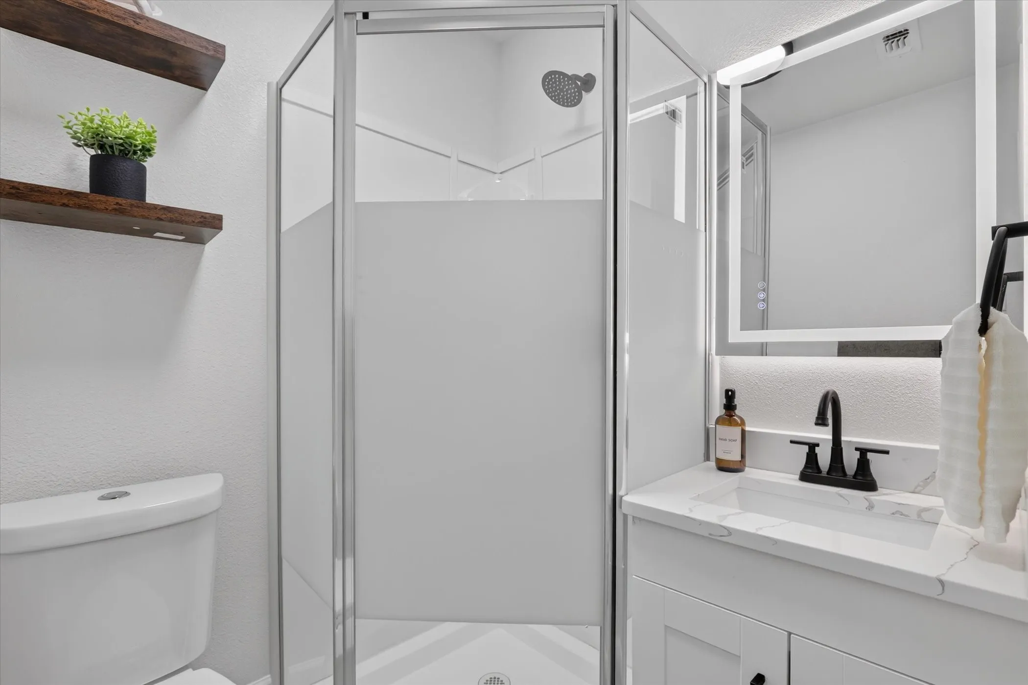 Shower enclosure with frosted glass, showerhead, vanity with integrated sink, black-finish faucet, and an illuminated medicine cabinet