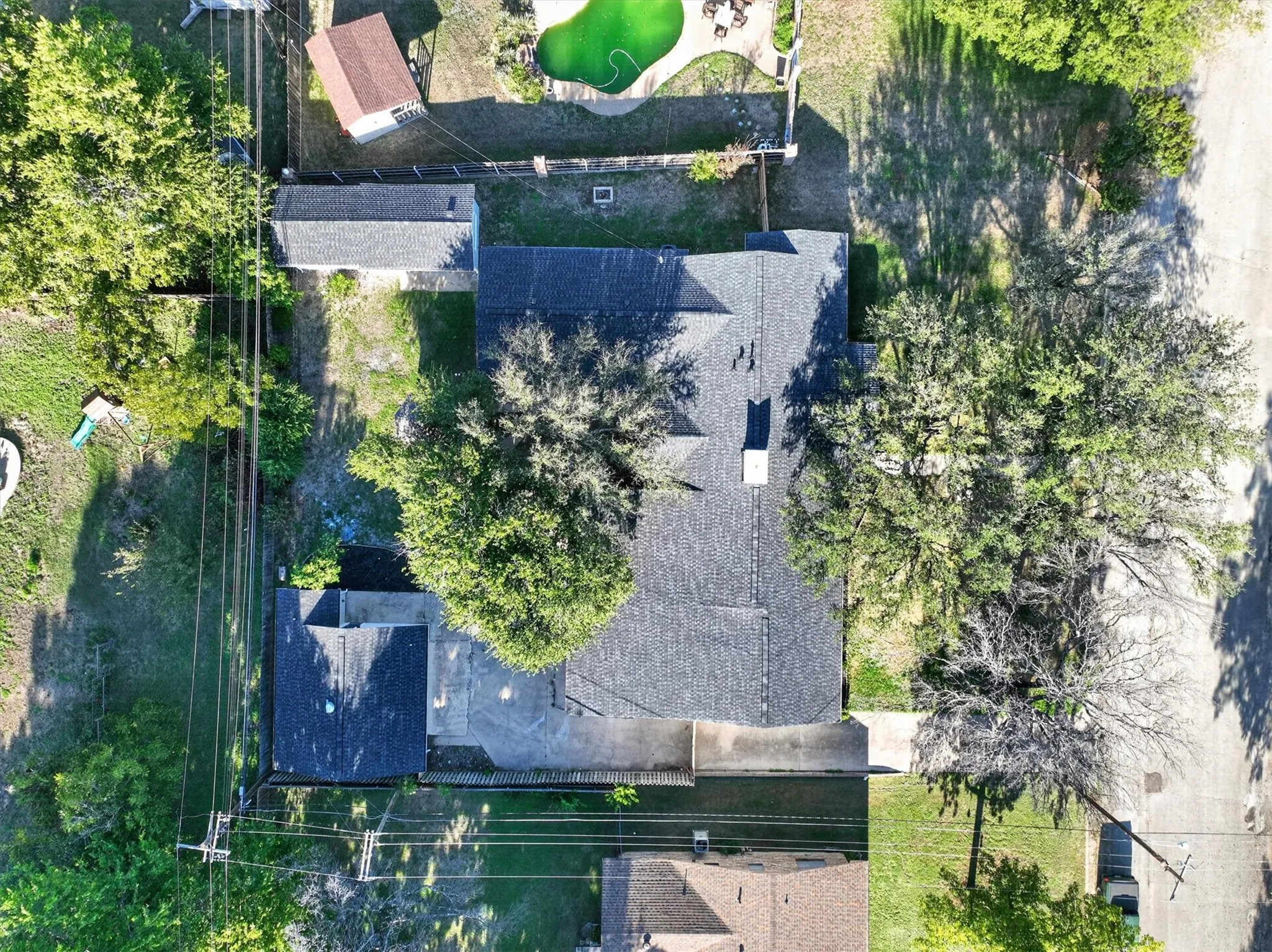 Asphalt shingle roof, mature trees, concrete driveway, and a detached structure