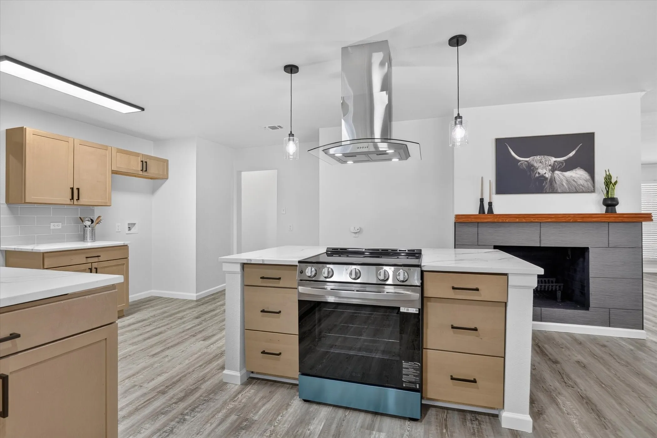 Kitchen island with built-in stainless steel range, stainless steel range hood, light wood-finish cabinetry, white countertops, and wood-finish flooring