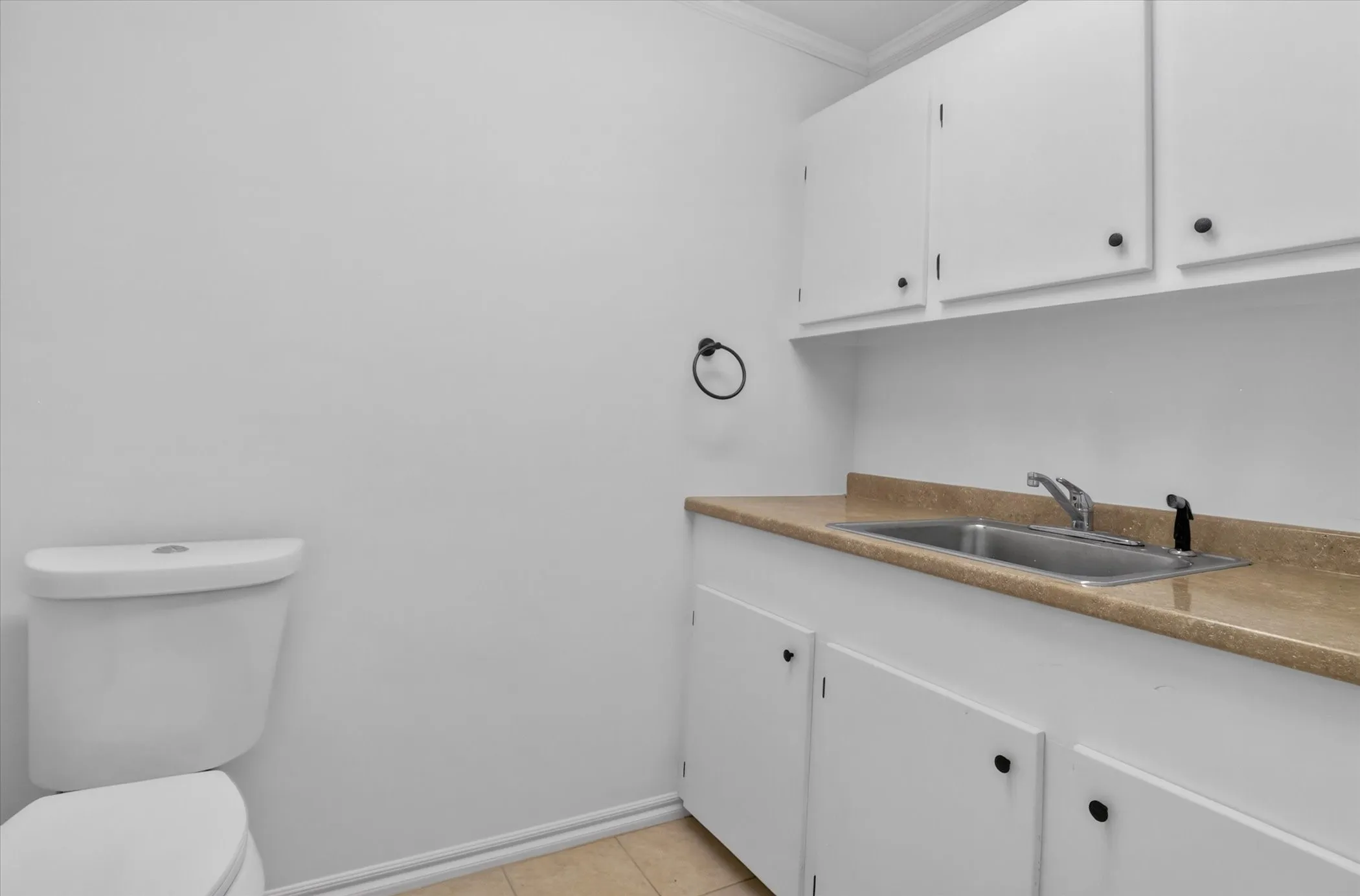White cabinetry with matte black hardware, integrated stainless steel sink, beige countertop, and tile flooring