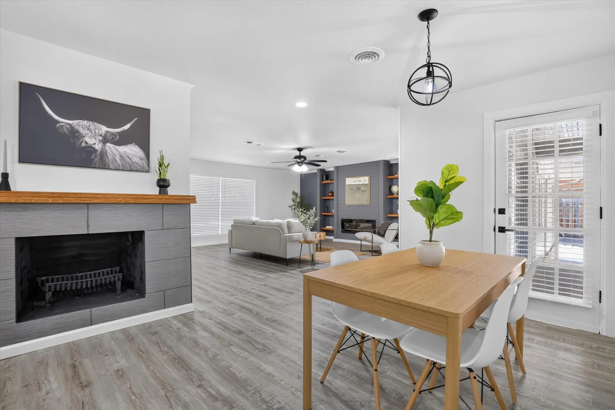 Light wood-finish dining table with a black orb pendant light, wood-finish flooring, and a fireplace with a wood mantel