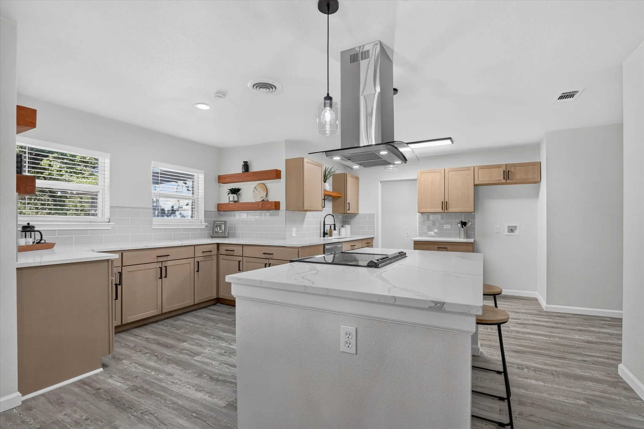 Kitchen featuring an island with a built-in cooktop, a stainless steel range hood, light wood-finish cabinetry, white subway tile backsplash, and wood-finish flooring