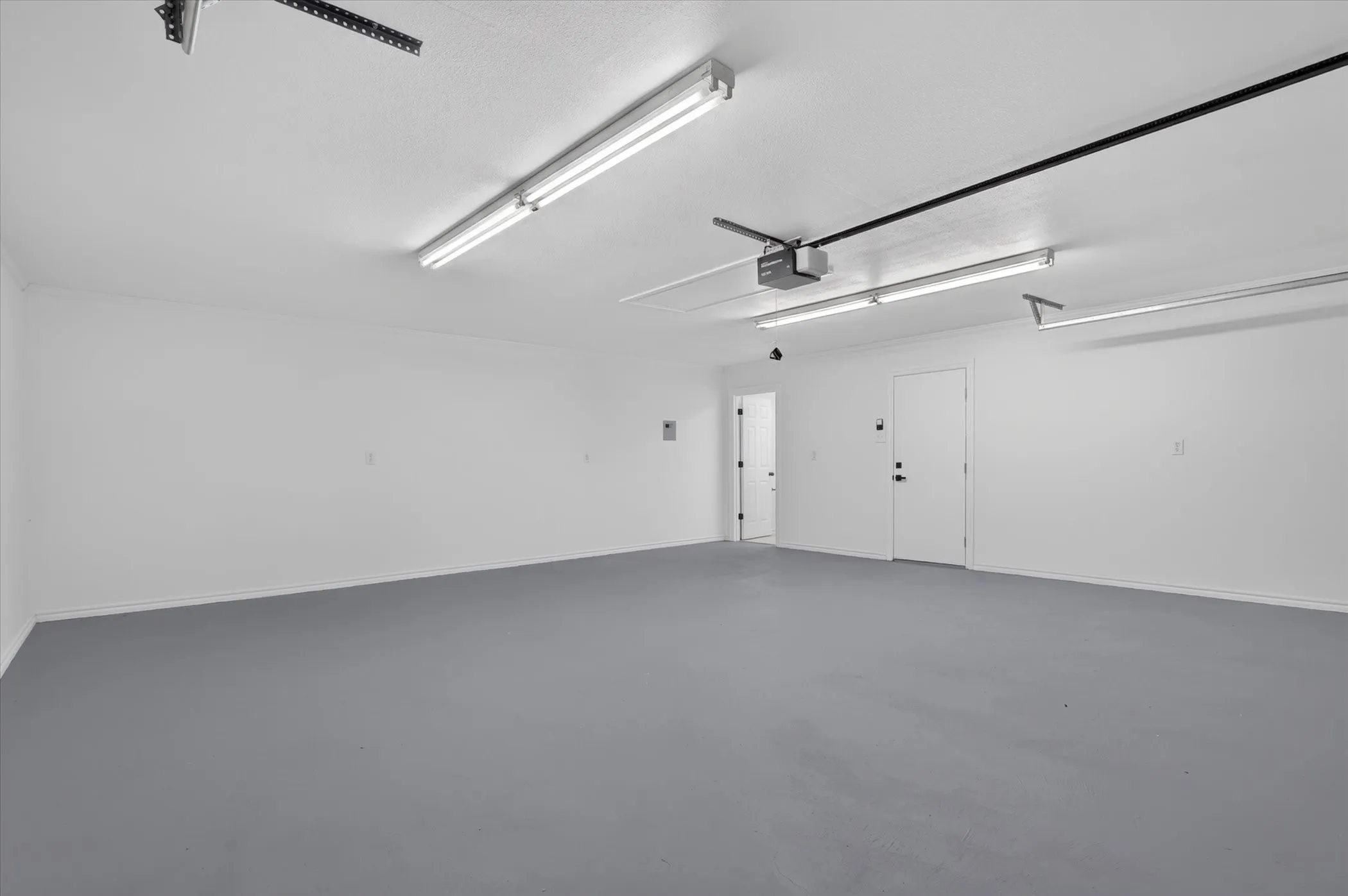 Spacious garage featuring a durable gray floor finish, multiple fluorescent light fixtures, and two interior access doors