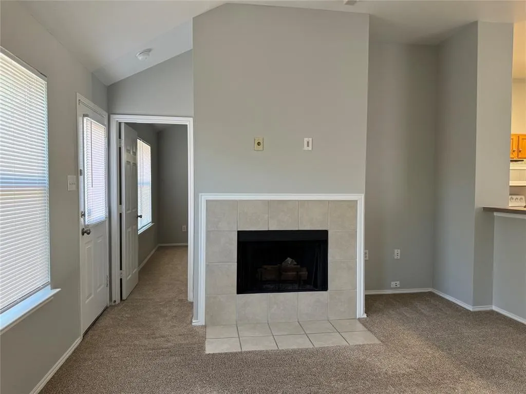 Carpeted living area featuring a tile-surrounded fireplace and vaulted ceiling