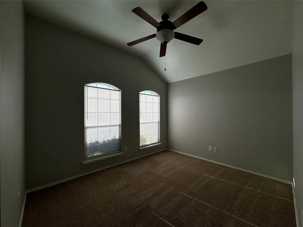 Vaulted ceiling with a ceiling fan, two arched windows with blinds, and carpeted flooring