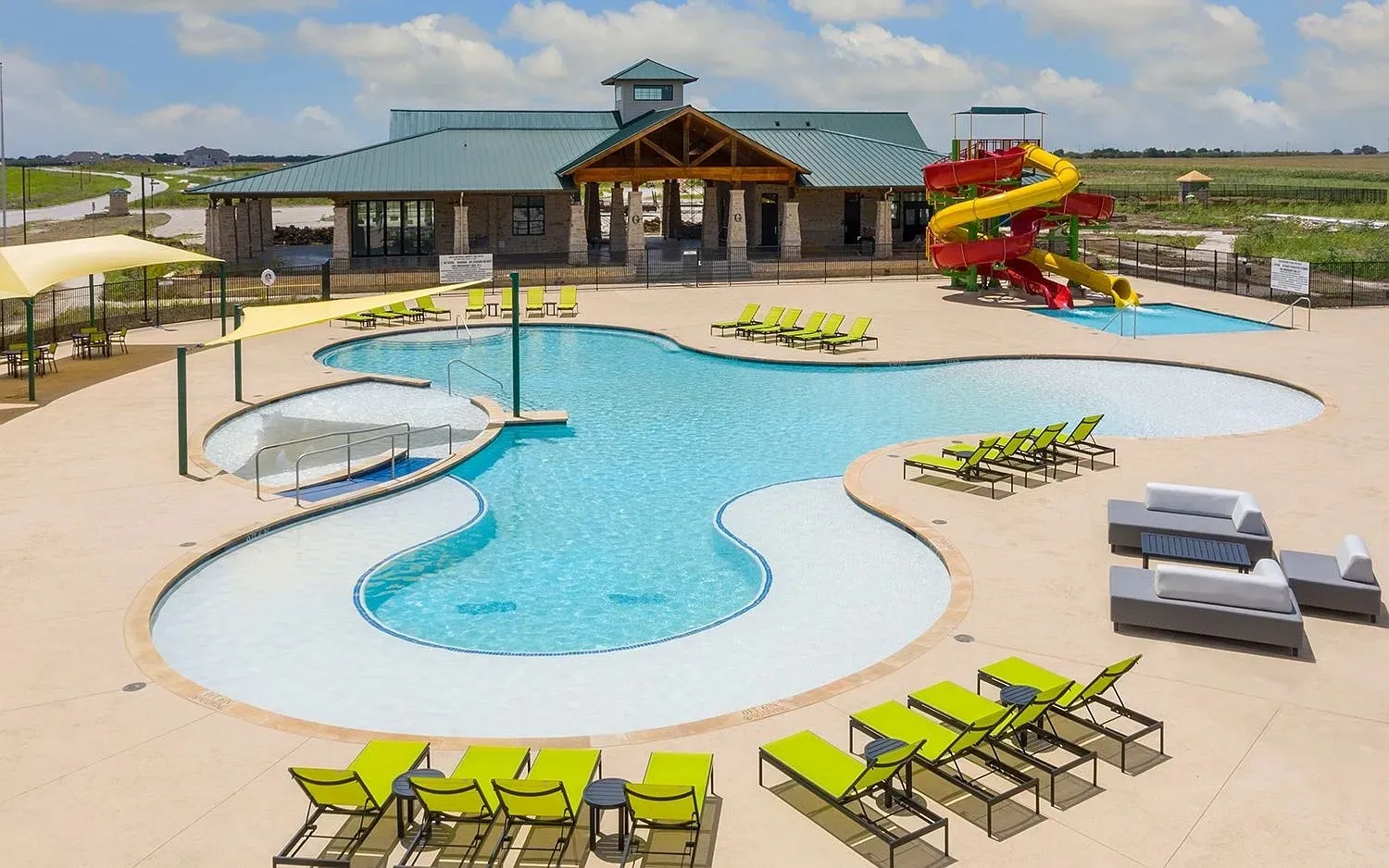 Resort-style pool area featuring a freeform swimming pool with a shallow entry, an integrated splash pad, and a separate aquatic play structure with waterslides