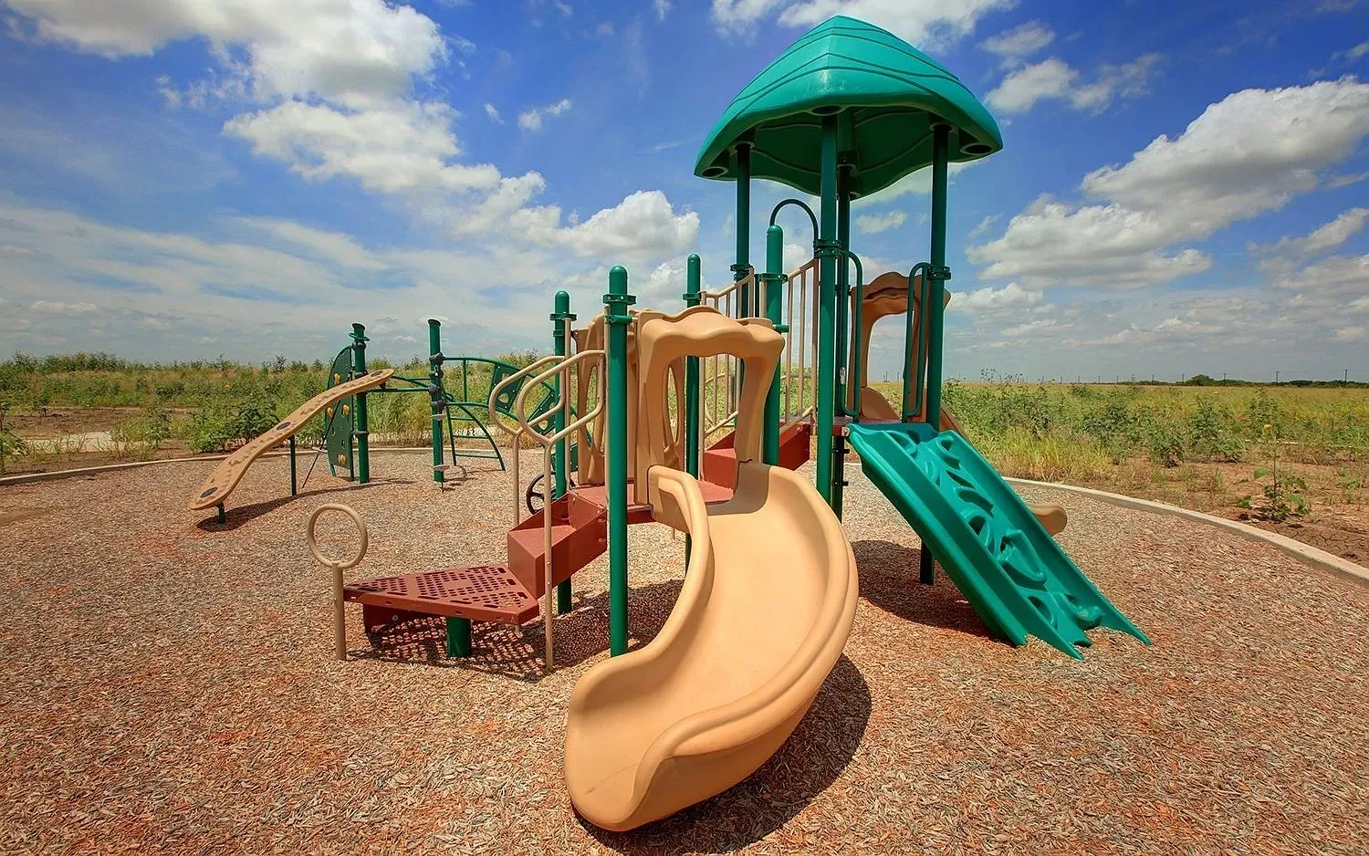 Community playground featuring a multi-level play structure, two slides, climbing elements, and a canopy