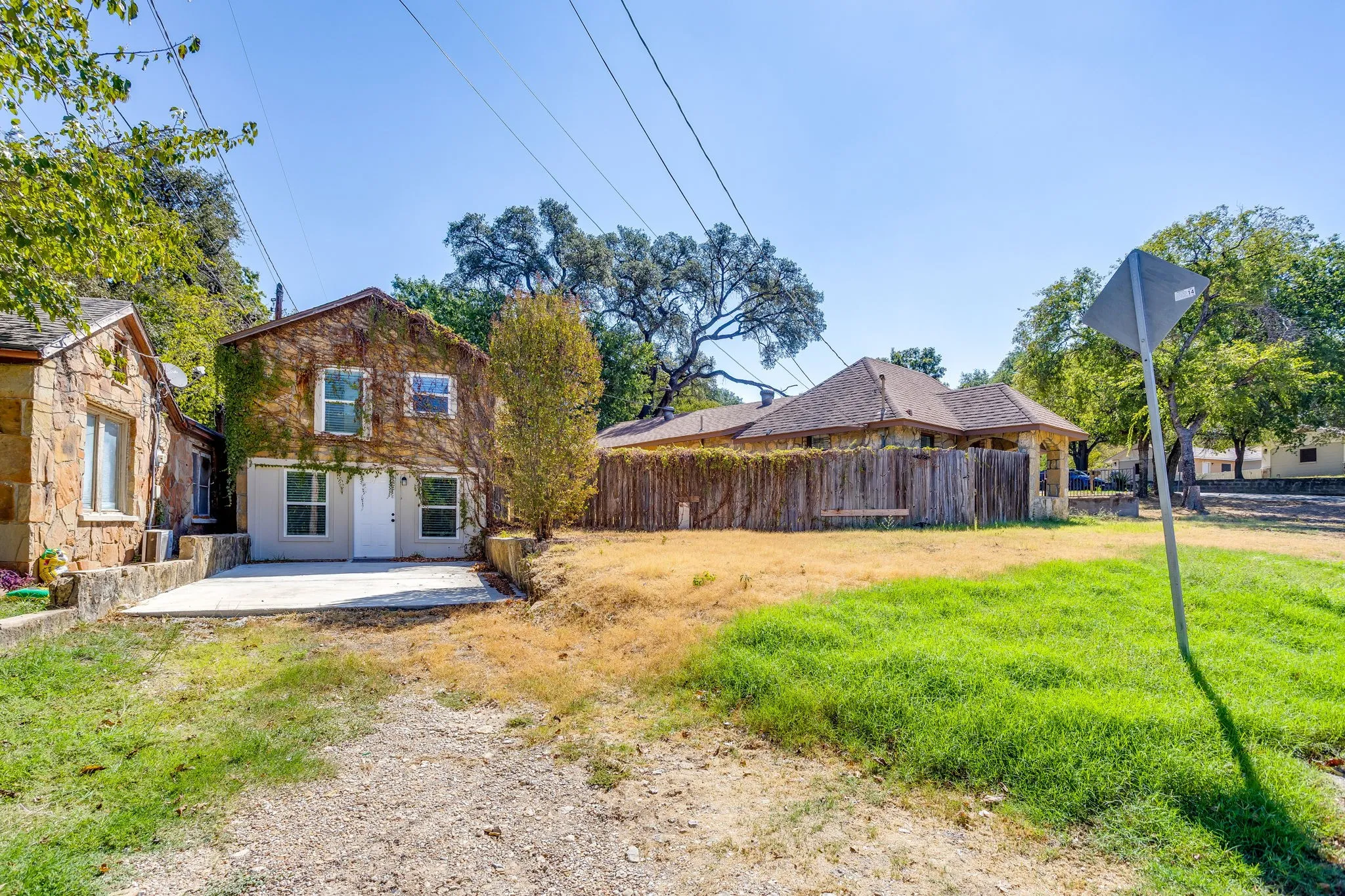 Stone exterior architecture, wood fencing, multiple windows, established trees, concrete pad