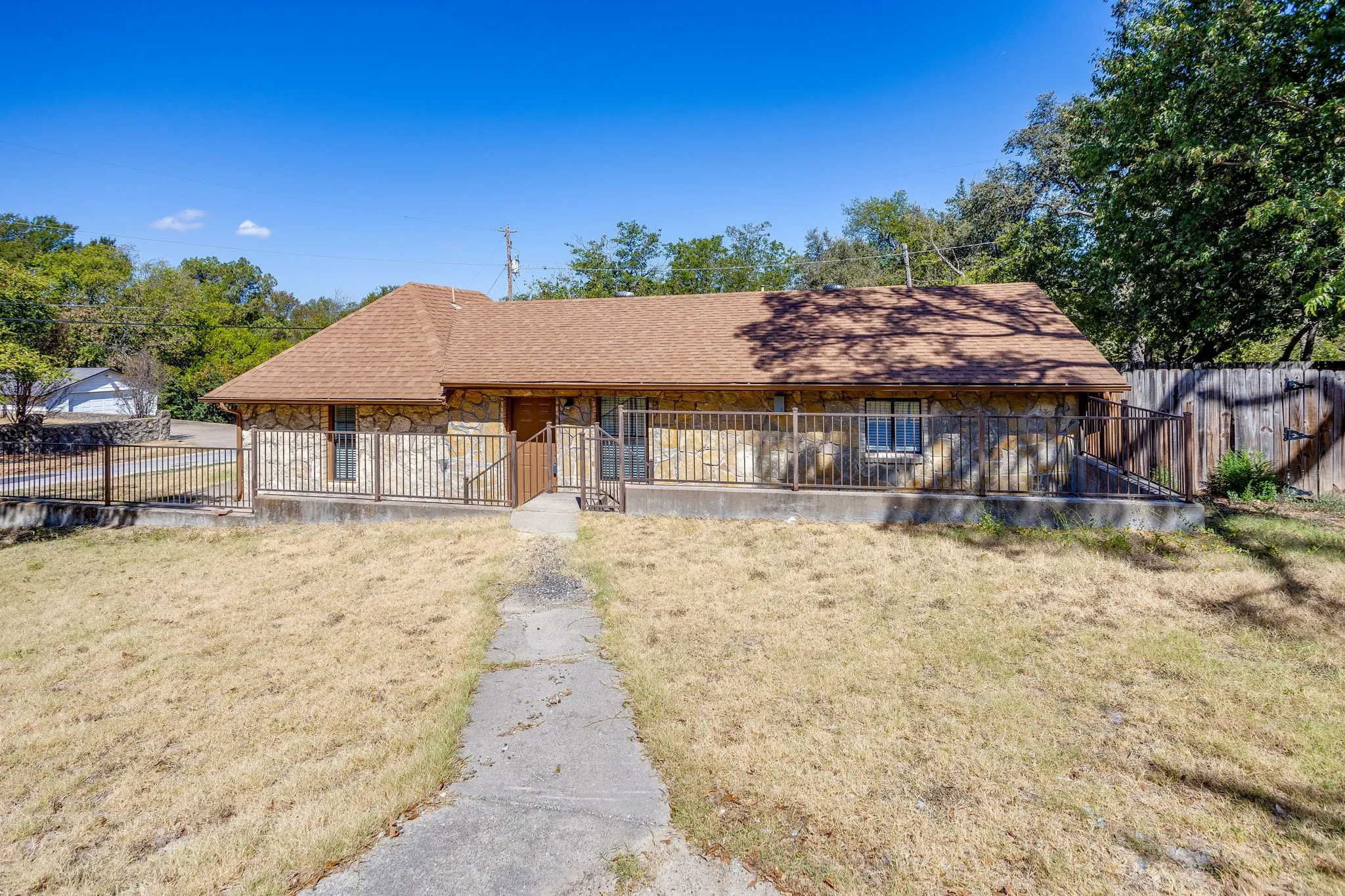 Stone veneer exterior with a brown shingle roof, front porch with black metal railings, and a concrete walkway
