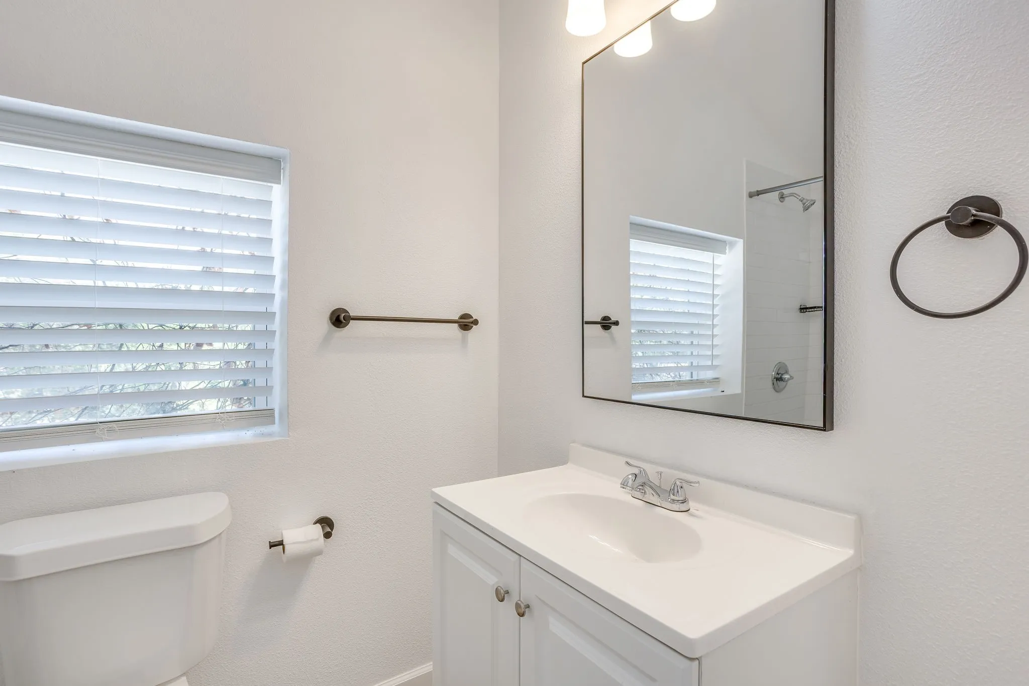 White vanity with integrated sink, chrome faucet, framed mirror, and window with blinds